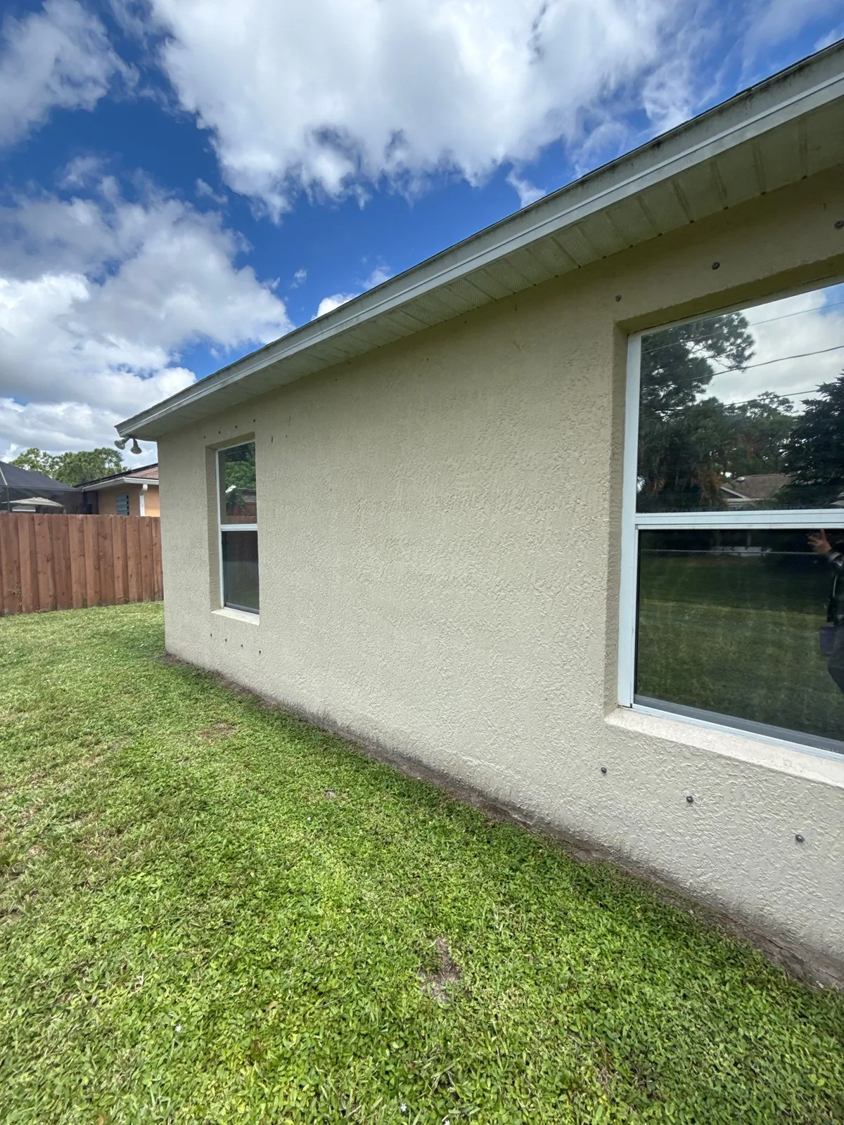Exterior Painting in Bayside Lakes, Florida. Side elevation of a single-storey beige stucco house with white window trim and white fascia under a blue sky.