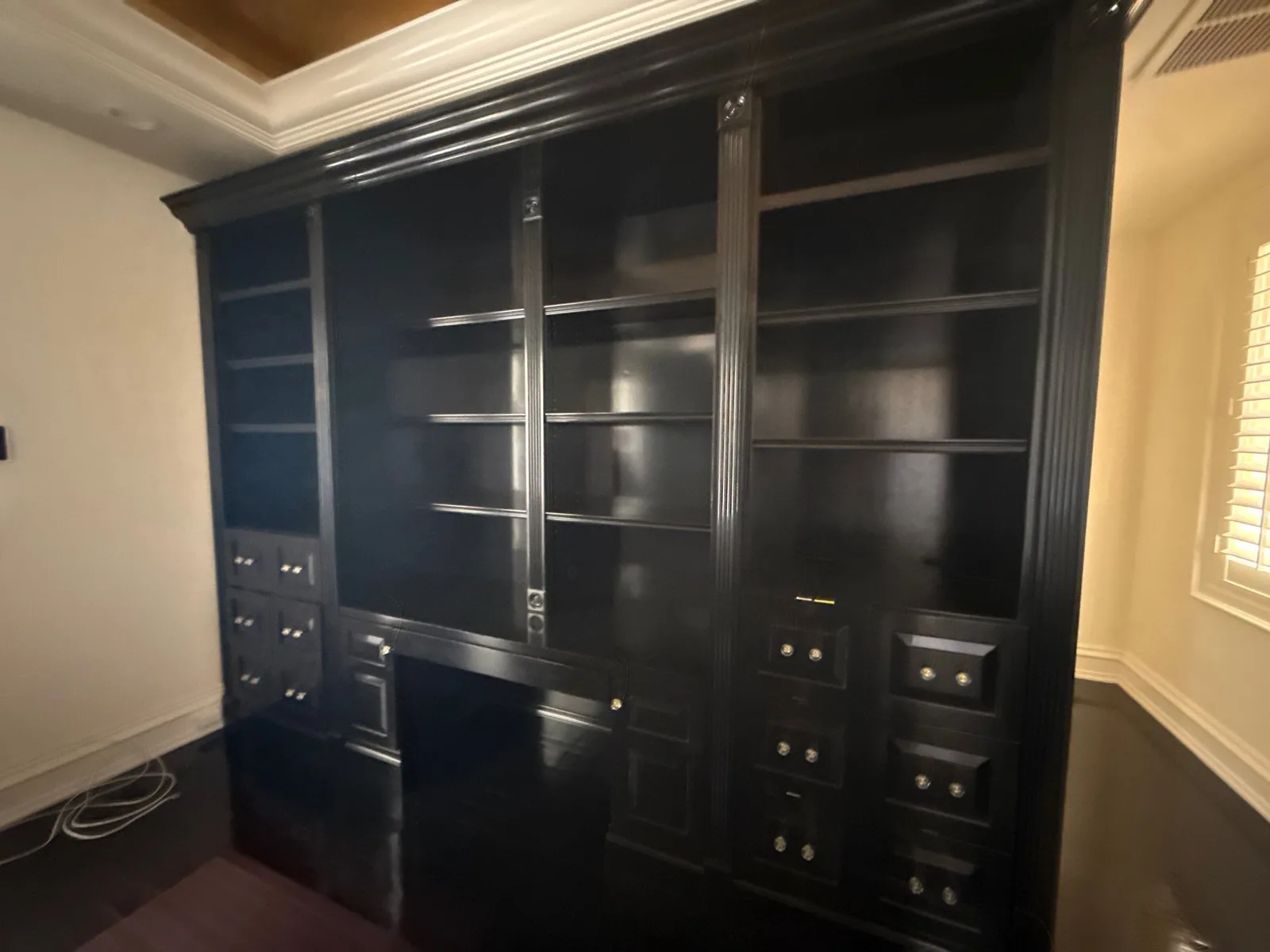 Cabinet Refinishing in Boca Raton, Florida. Large black lacquered built-in bookcase with open shelves, glass-front upper cabinets and a bank of drawers in an empty room.