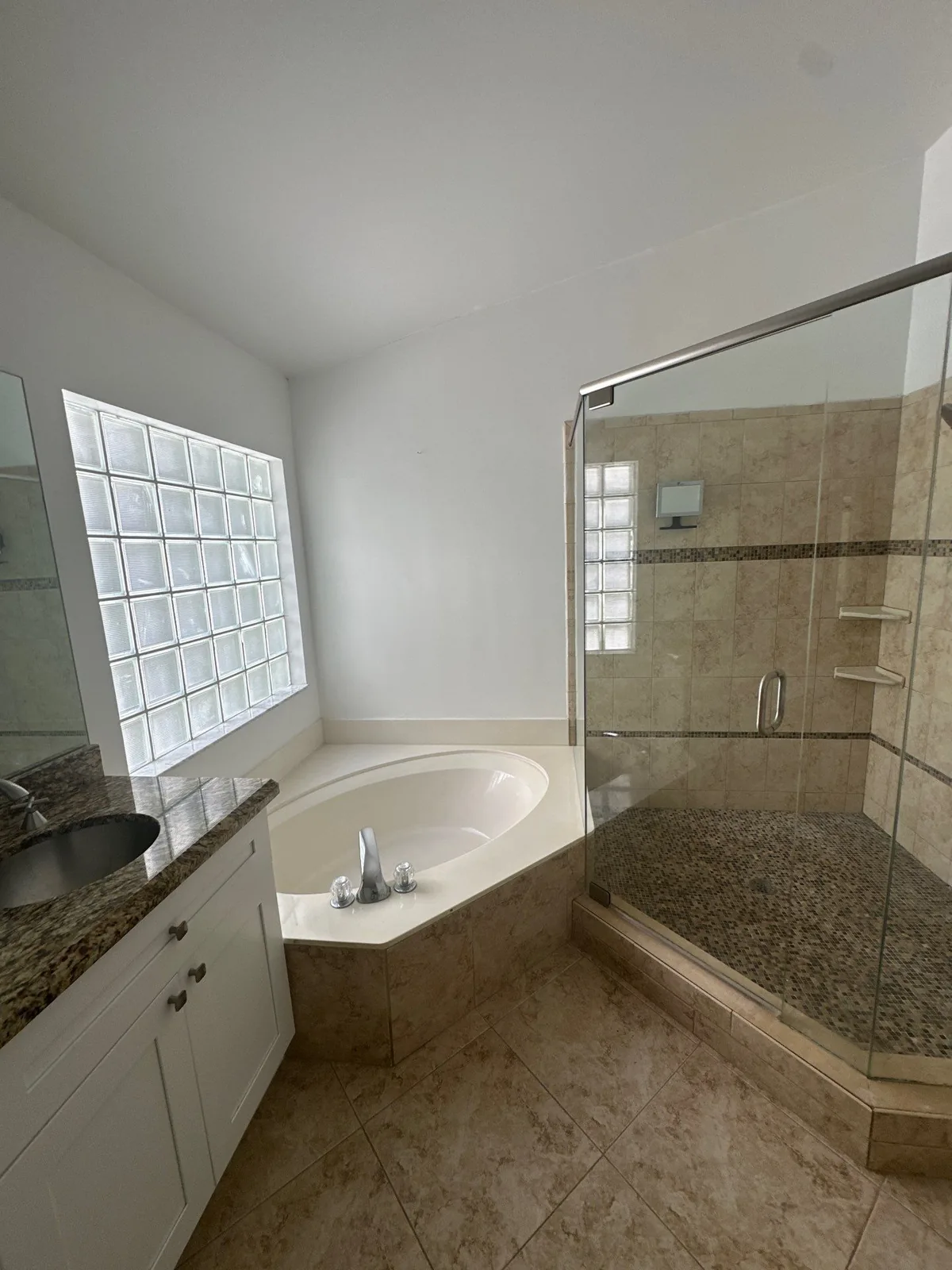 Interior Painting in Delray Beach, Florida. Bathroom with white walls, corner soaking tub, glass block window, tiled shower enclosure and white vanity.
