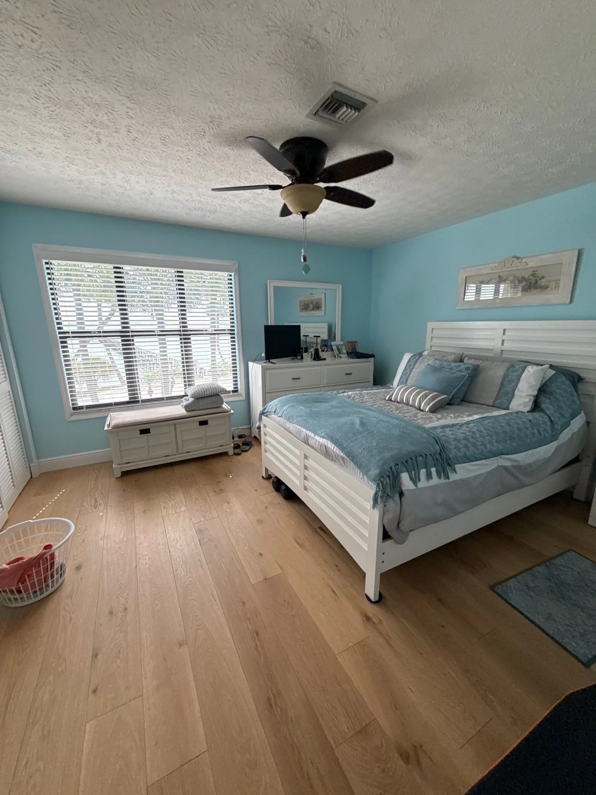 Interior Painting in Eden, Florida. Bedroom with light blue painted walls, white bed and dresser, ceiling fan and wood flooring.