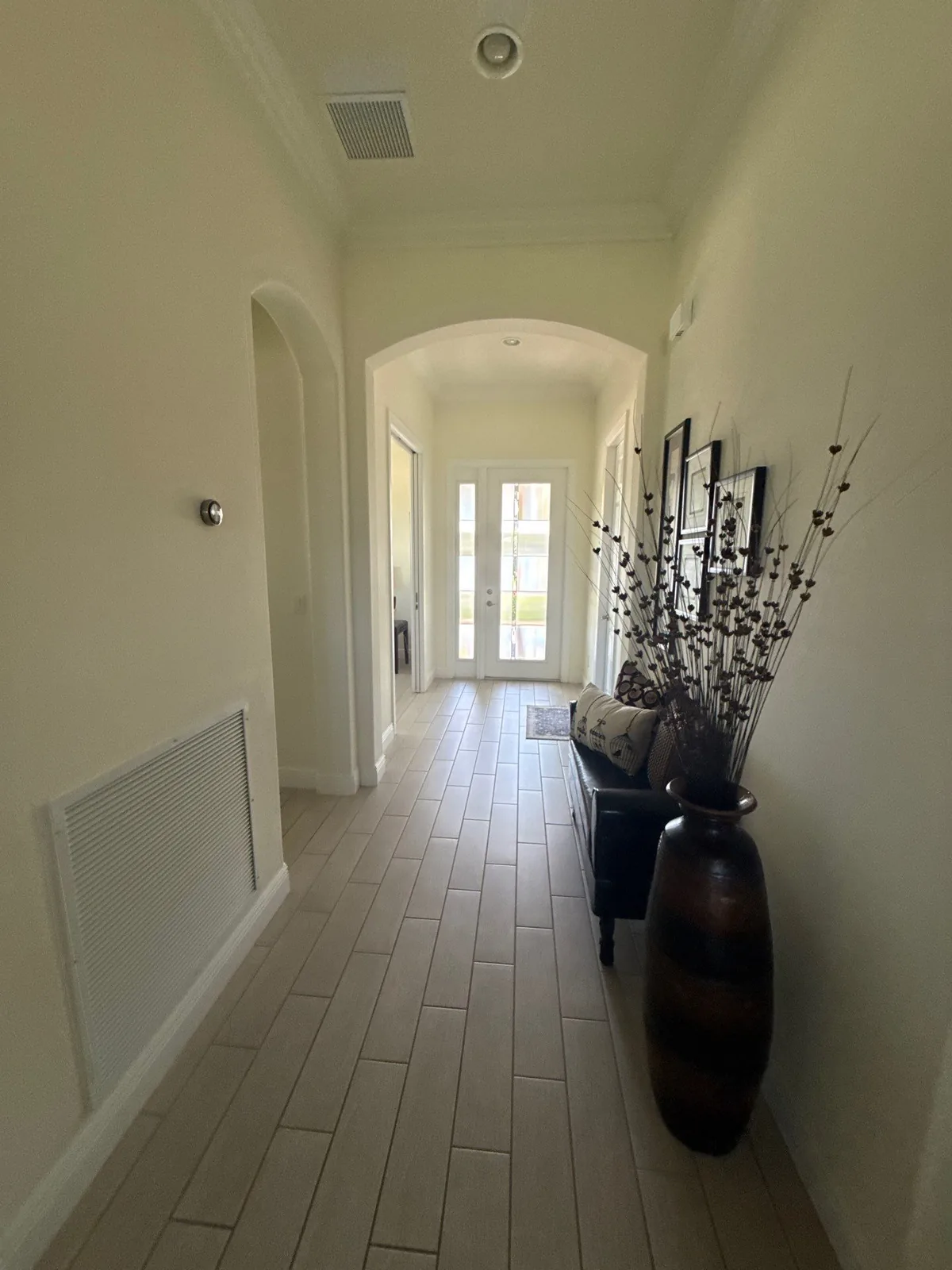 Interior Painting in Florida Ridge, Florida. Entry hallway with painted walls and crown moulding, arched opening, tile floor and a tall decorative vase, looking toward the front door.