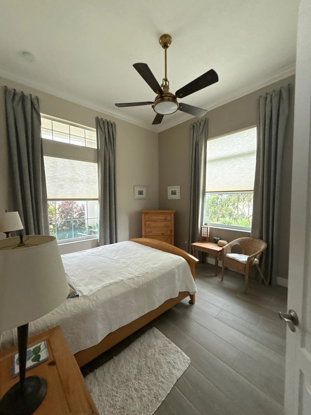 Interior Painting in Florida Ridge, Florida. Bedroom with greige walls, white crown moulding, two curtained windows, ceiling fan and made bed.