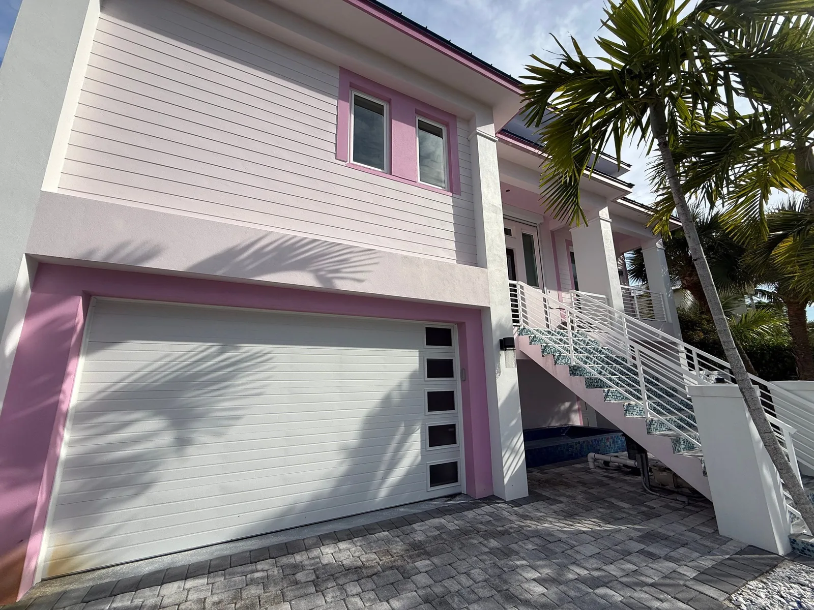 Exterior Painting in Fort Pierce, Florida. Two-storey coastal home painted pink and white with white garage door, exterior stair and palms.