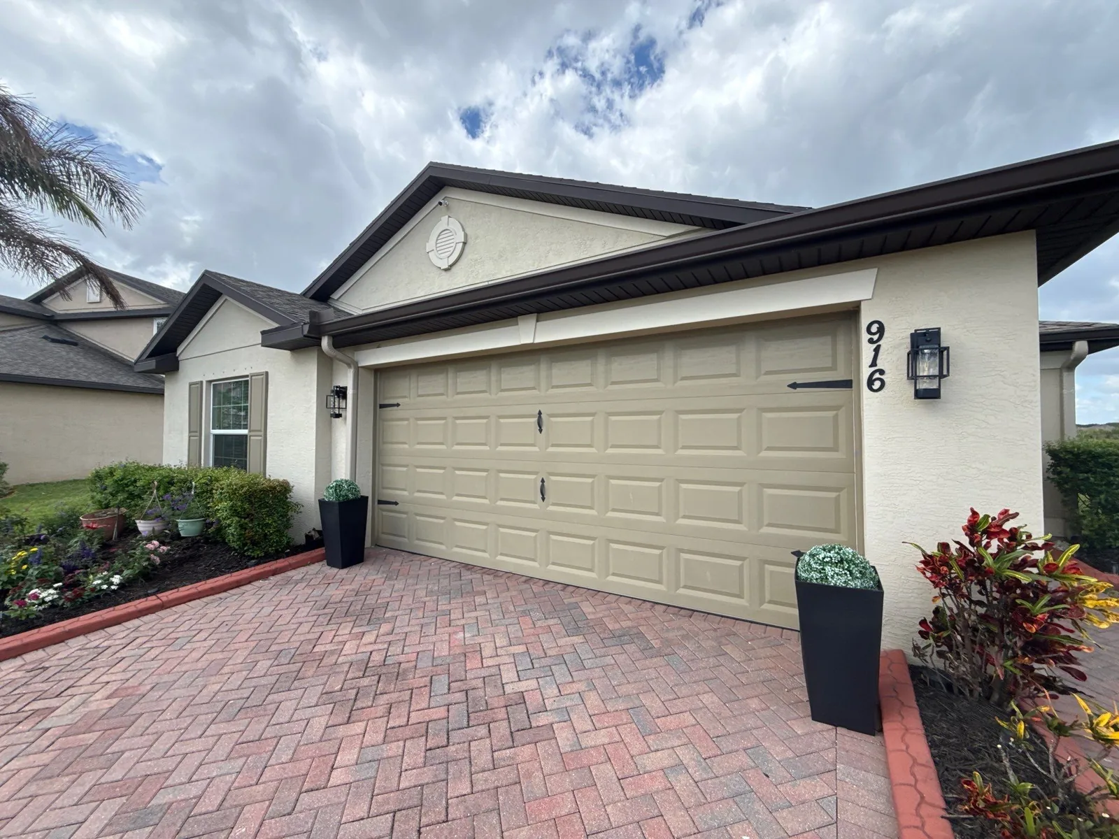 Exterior Painting in Fort Pierce, Florida. Single-storey house front, cream stucco with dark brown fascia and tan garage door, brick paver driveway.