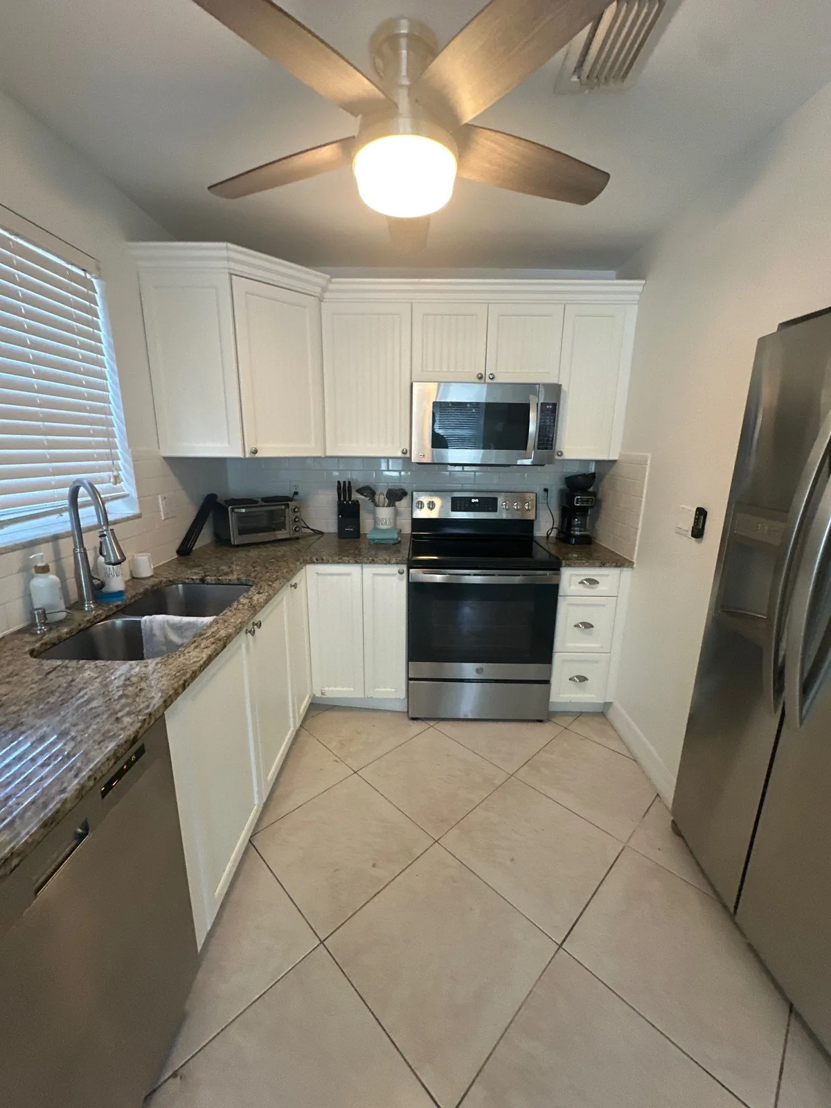 Cabinet Refinishing in Fort Pierce Shores, Florida. Kitchen with white cabinets, speckled granite counters, tile backsplash and stainless steel appliances.