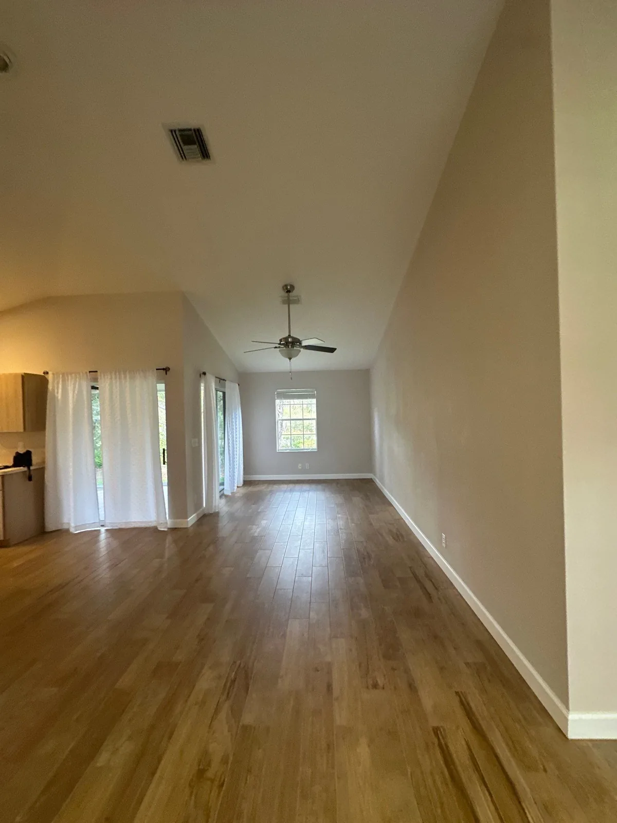 Interior Painting in Fruita, Florida. Empty living room with vaulted ceiling, ceiling fan, greige walls, white trim and wood-look floor.