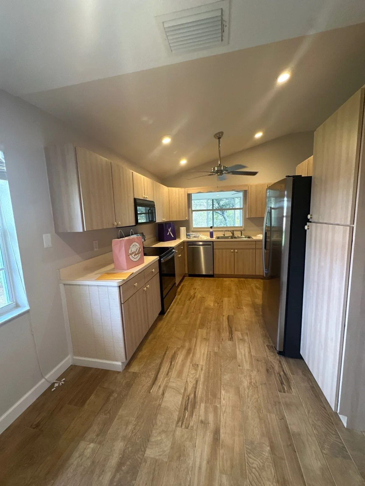 Interior Painting in Fruita, Florida. Kitchen with light wood-tone cabinets, vaulted ceiling with recessed lights and ceiling fan, stainless dishwasher and wood-look floor.