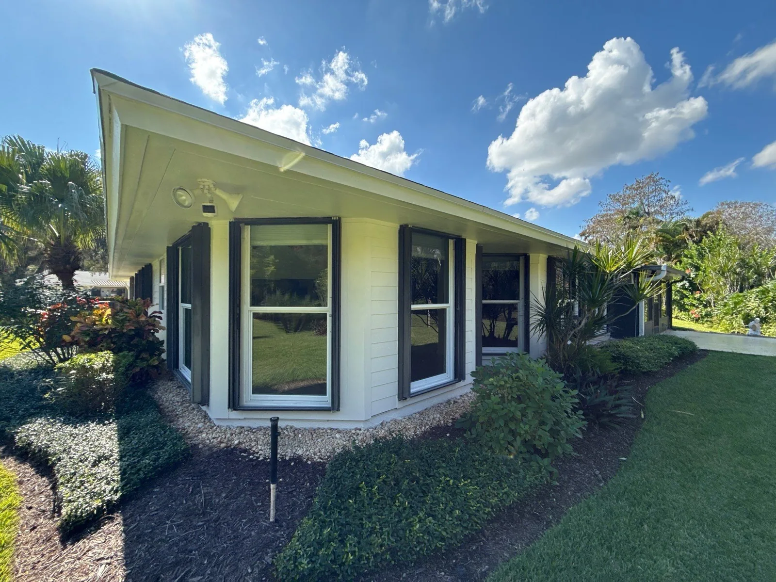 Exterior Painting in Hobe Sound, Florida. Front corner of a single-storey home, white exterior with dark window trim and a bay window, under blue sky.
