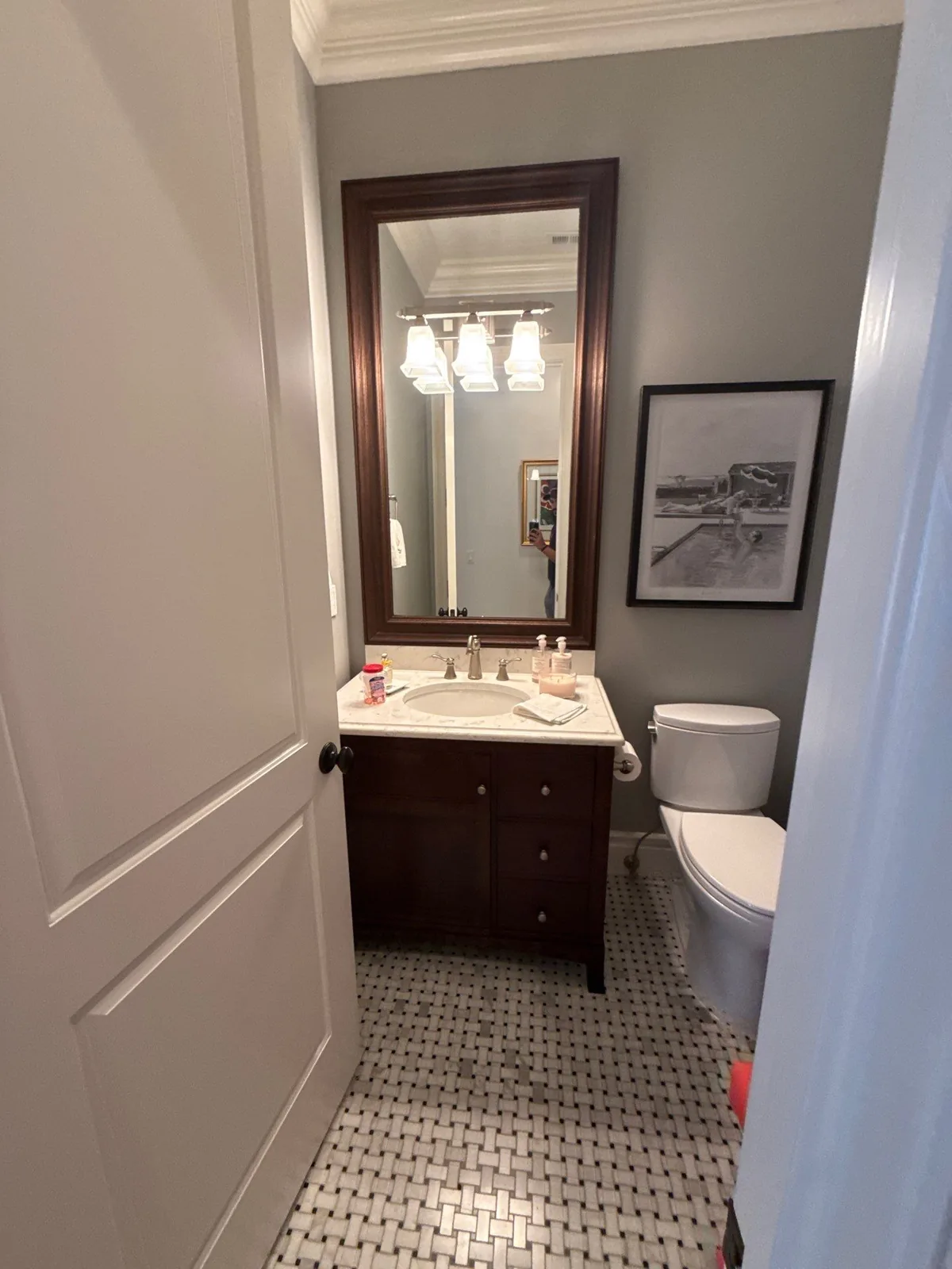 Interior Painting in Indian River Shores, Florida. Powder room with grey painted walls, dark wood vanity and framed mirror over mosaic tile floor.