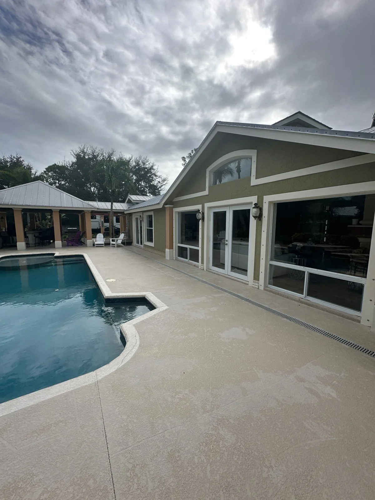 Exterior Painting in Jensen Beach, Florida. Single-storey home exterior in olive green with white trim, viewed across a pool and light-coloured pool deck.