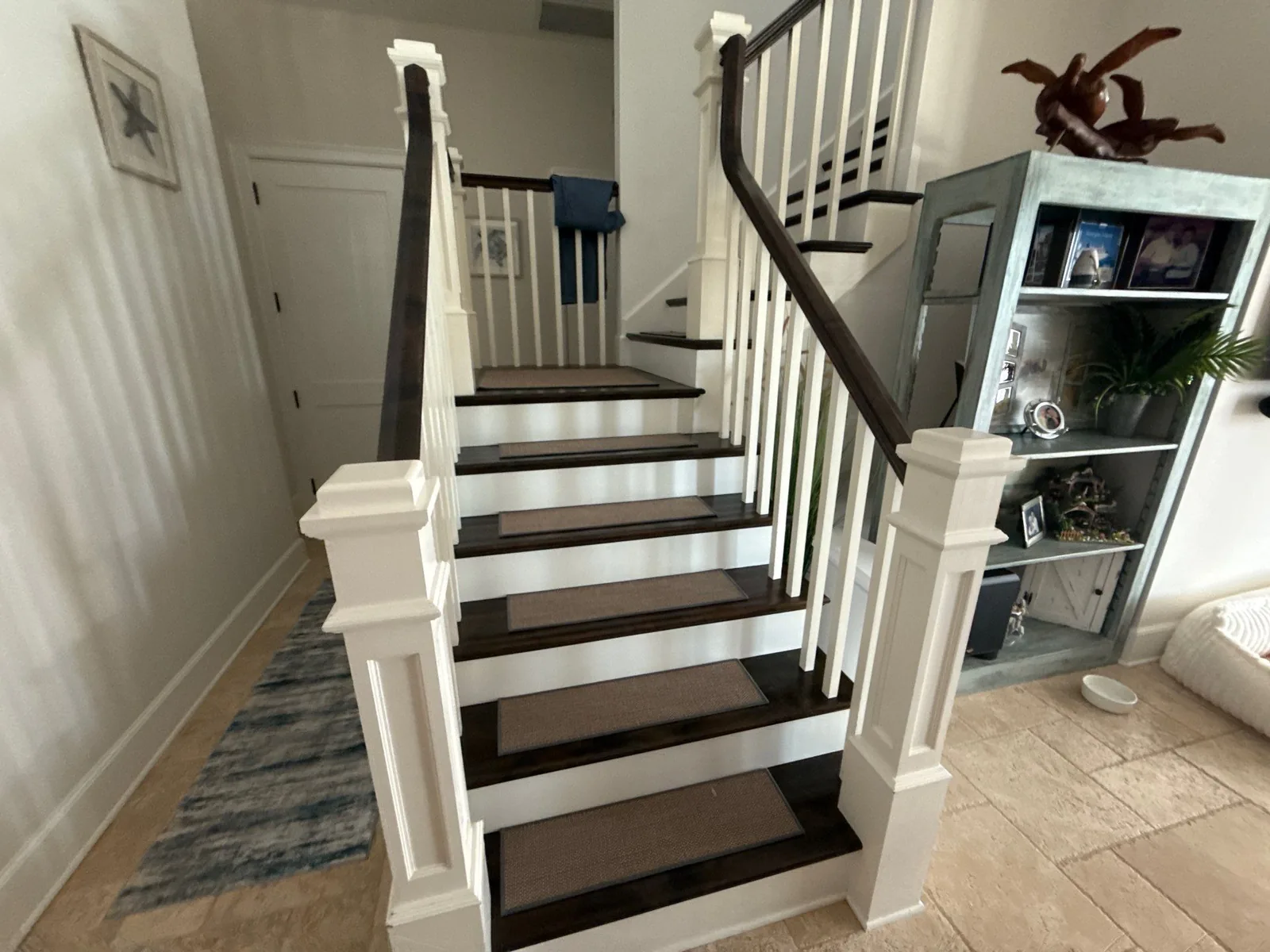 Interior Painting in Jensen Beach, Florida. Interior staircase with white-painted newel posts, balusters and risers against stained wood treads and handrail, cream walls.
