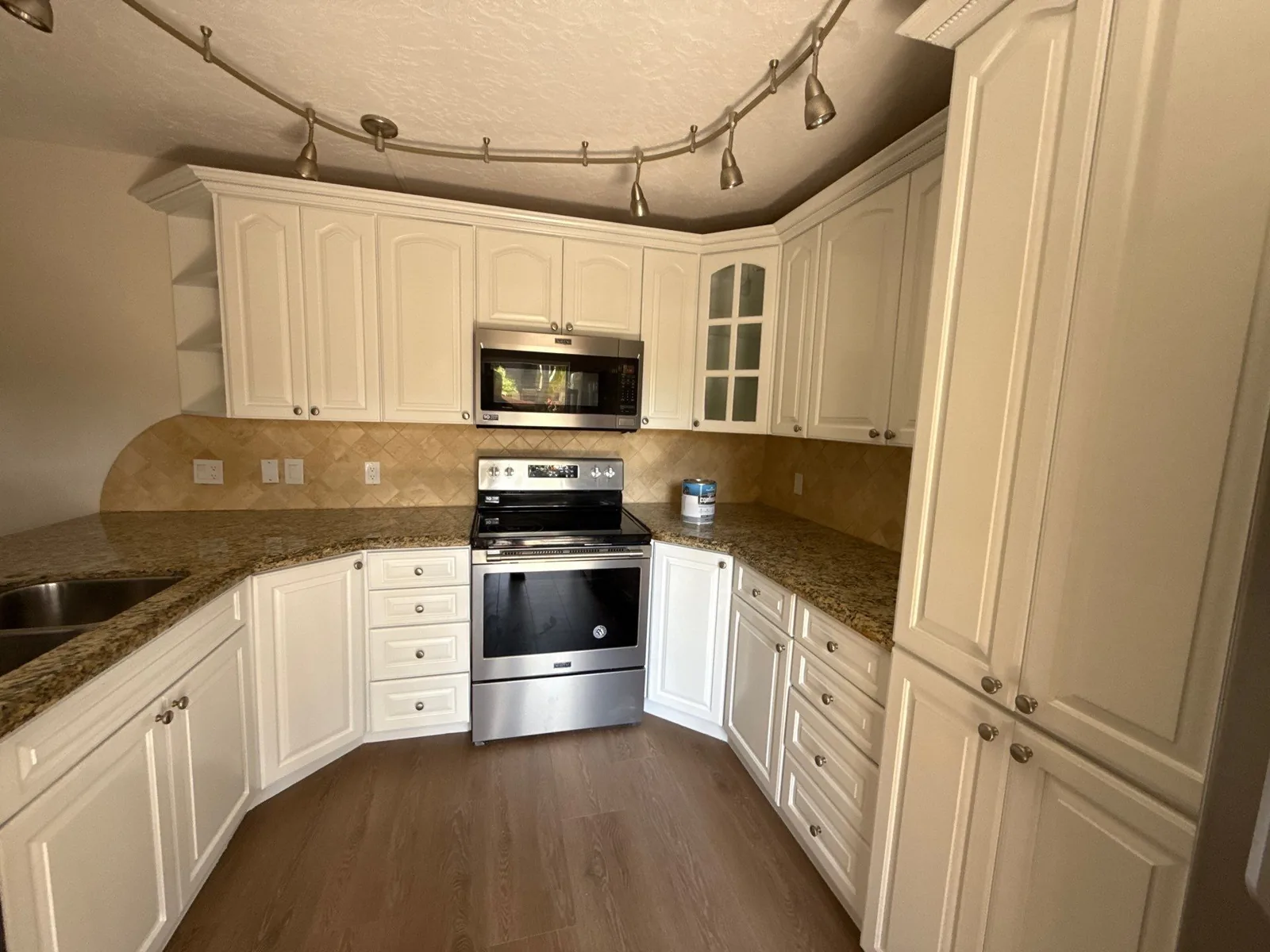 Cabinet Refinishing in Juno Beach, Florida. Kitchen with cream raised-panel cabinets, stainless range and microwave, tile backsplash and track lighting.