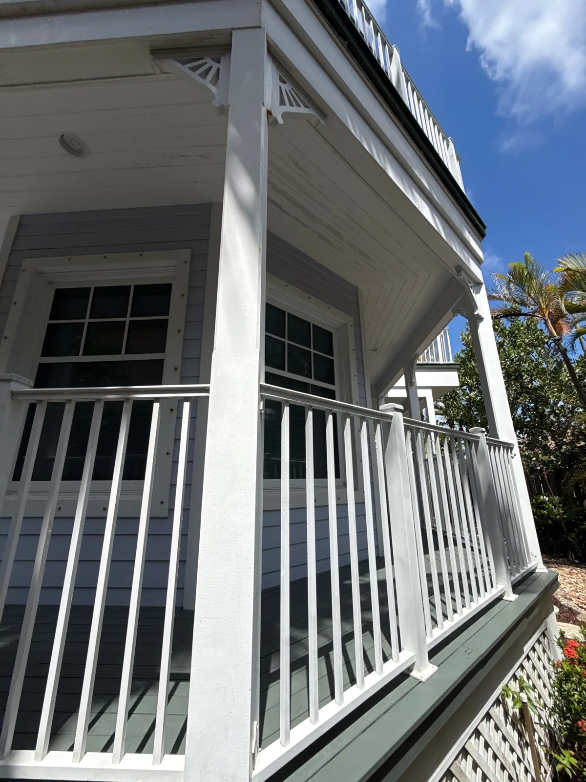 Exterior Painting in Juno Beach, Florida. Second-storey balcony with white railing, white decorative brackets and trim, pale grey lap siding and green painted decking.