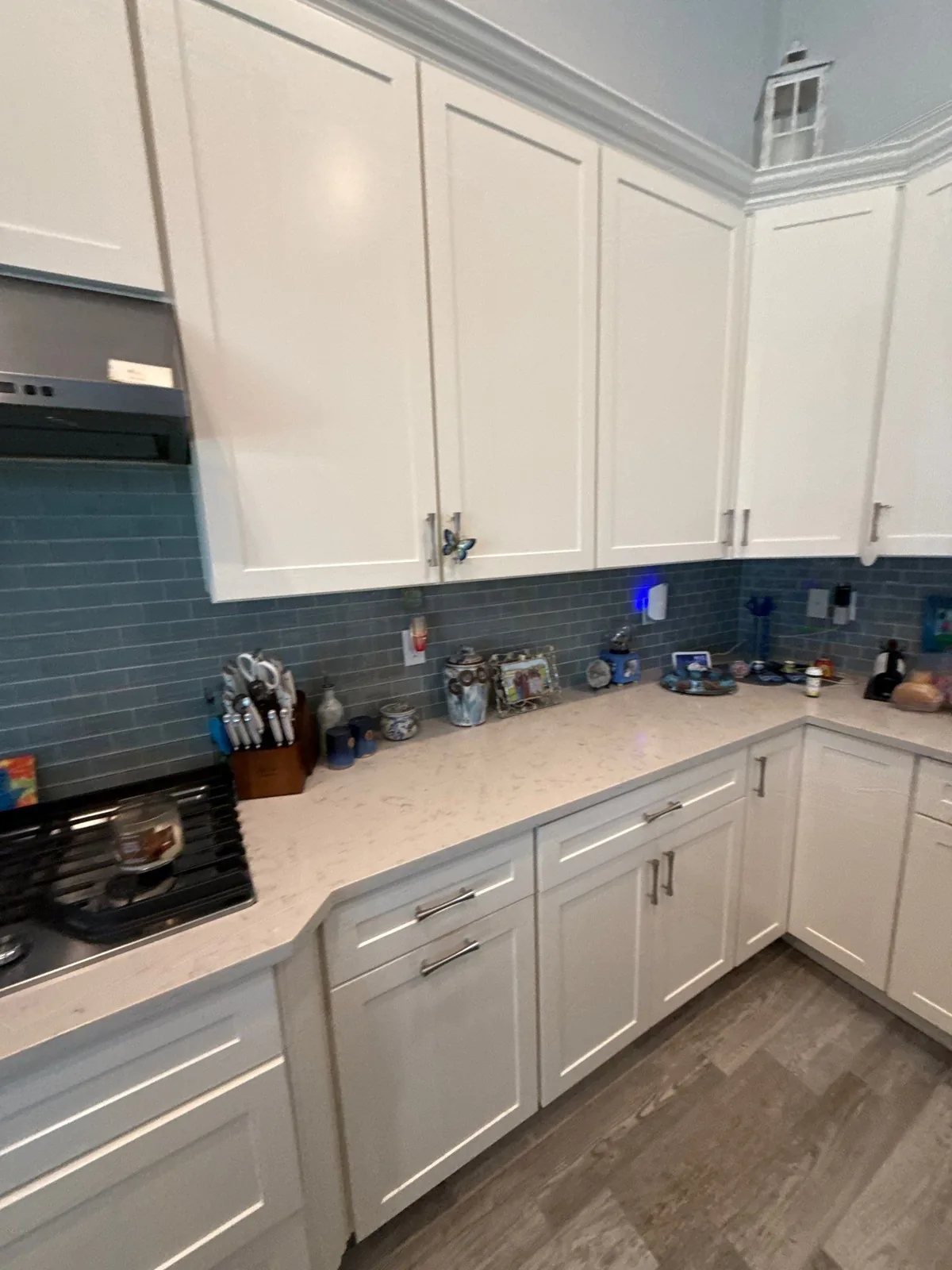 Cabinet Refinishing in Jupiter, Florida. White kitchen cabinets with shaker-style doors, blue subway tile backsplash, light stone countertop and range hood.
