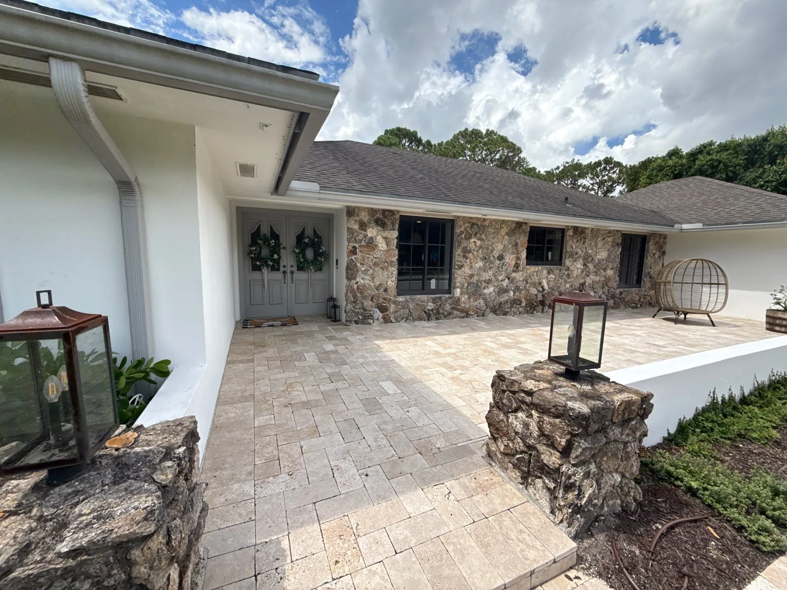 Exterior Painting in Jupiter, Florida. Single-storey home with white painted stucco and stone veneer, wreaths on the double entry doors, travertine paver courtyard.