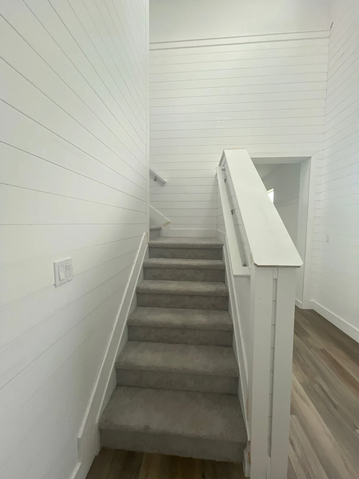 Interior Painting in Lakewood Park, Florida. Staircase with white painted shiplap walls and white handrail, carpeted treads and wood-look flooring.