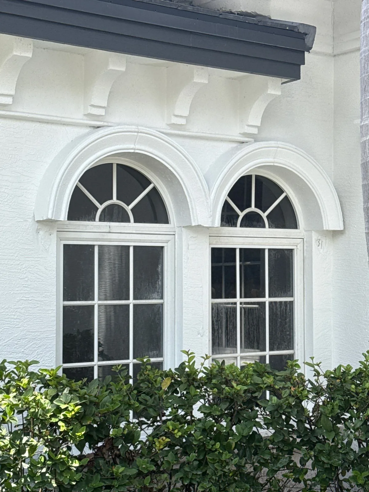 Exterior Painting in North Palm Beach, Florida. White stucco exterior wall with two arched windows, decorative corbels and dark fascia above.