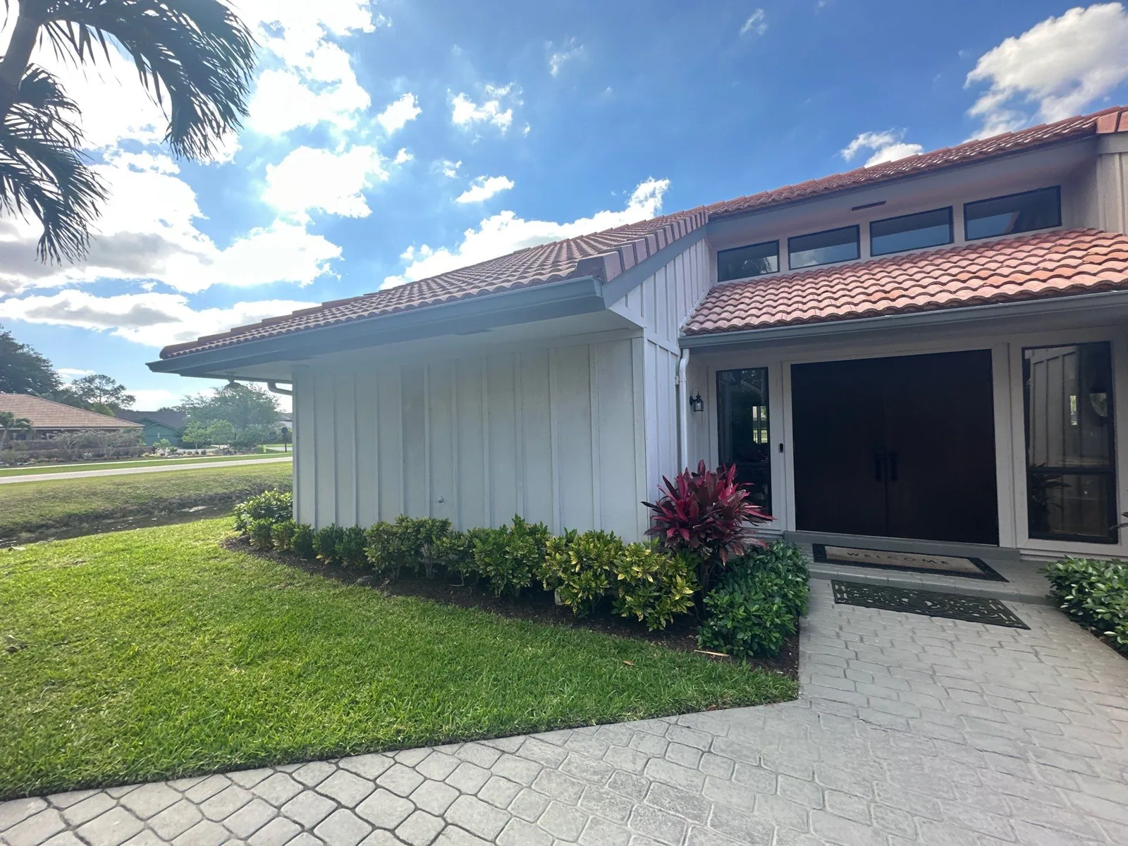 Exterior Painting in North Palm Beach, Florida. Side elevation and entry of a white-painted house with vertical board siding, barrel-tile roof and low hedges along the wall.