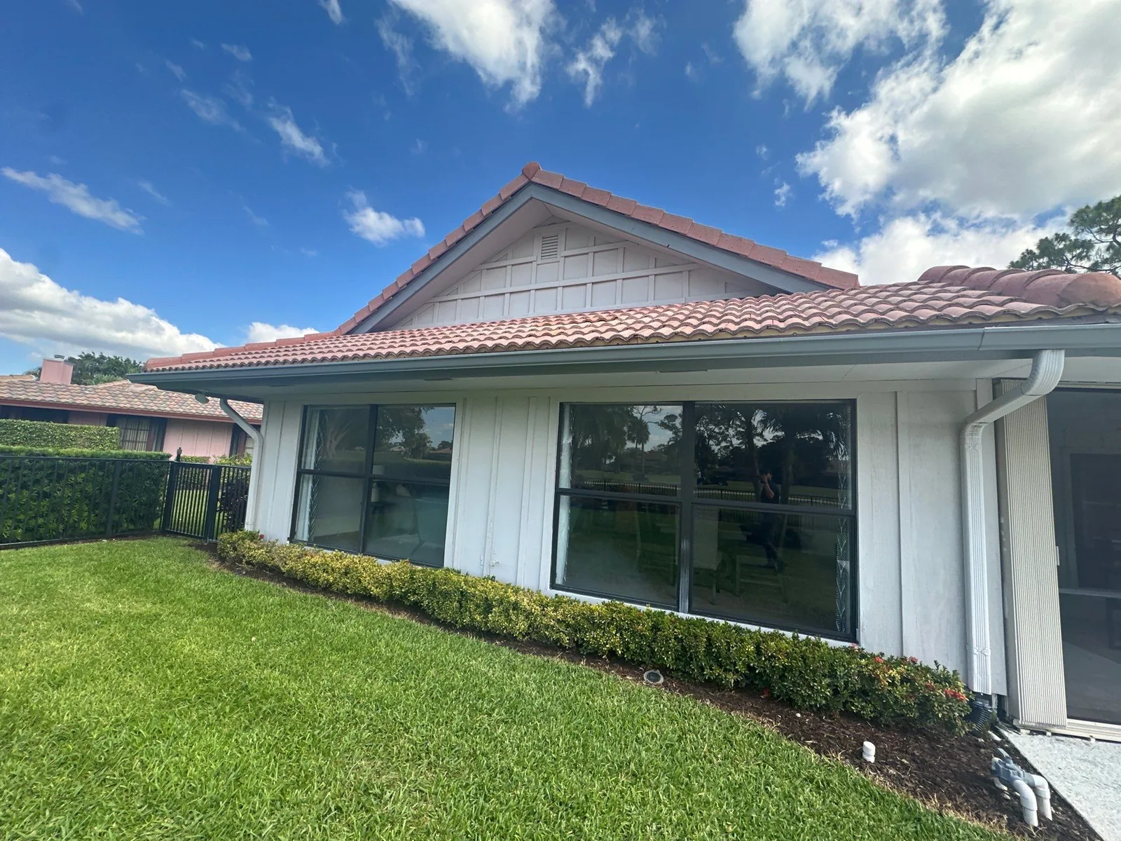 Exterior Painting in North Palm Beach, Florida. White-painted house exterior with large sliding glass windows, barrel-tile roof and a clipped hedge along the wall.