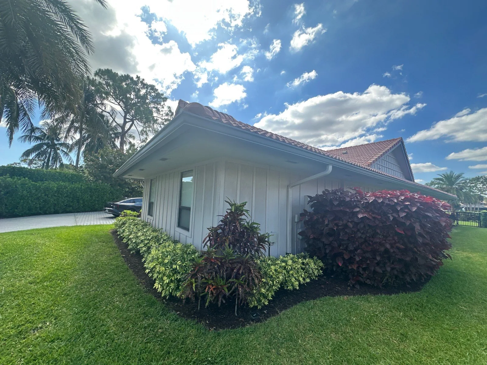 Exterior Painting in North Palm Beach, Florida. Corner of a single-storey home with white vertical board-and-batten siding, white soffit, barrel tile roof and landscaped planting beds.