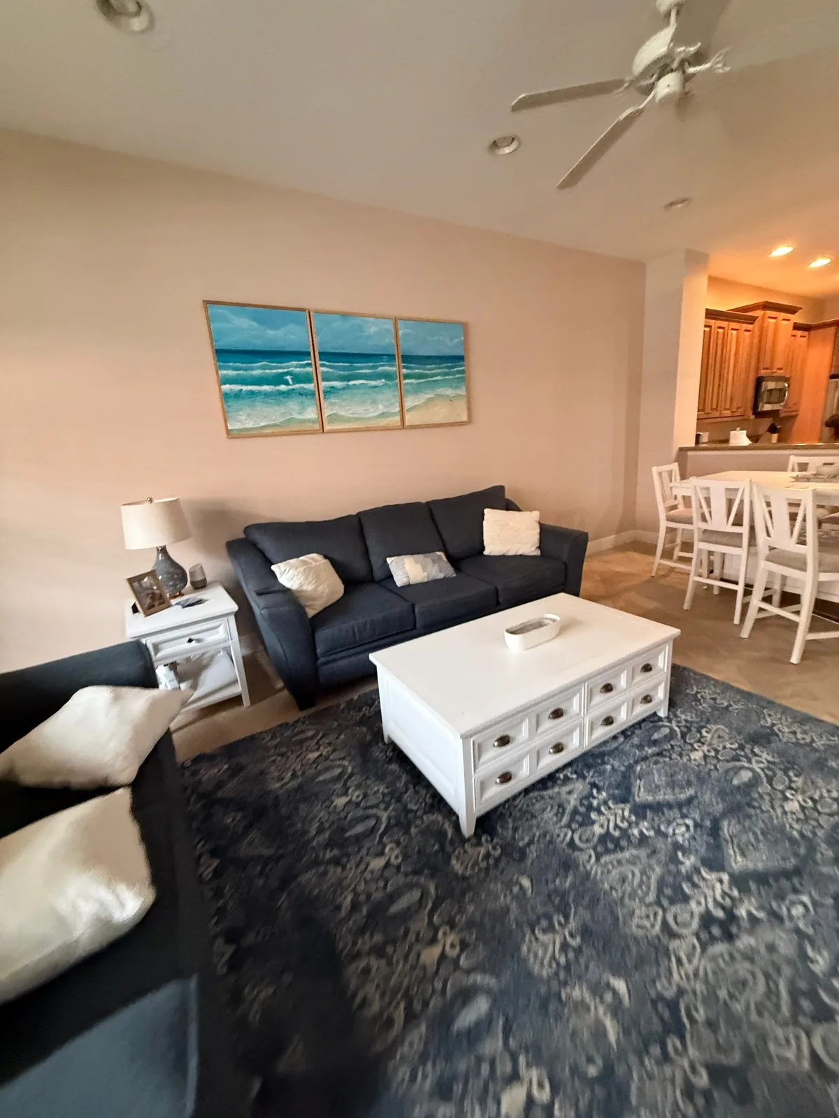 Interior Painting in North Palm Beach, Florida. Furnished living room with soft neutral painted walls and ceiling, navy sofa, coastal triptych artwork and a white coffee table.