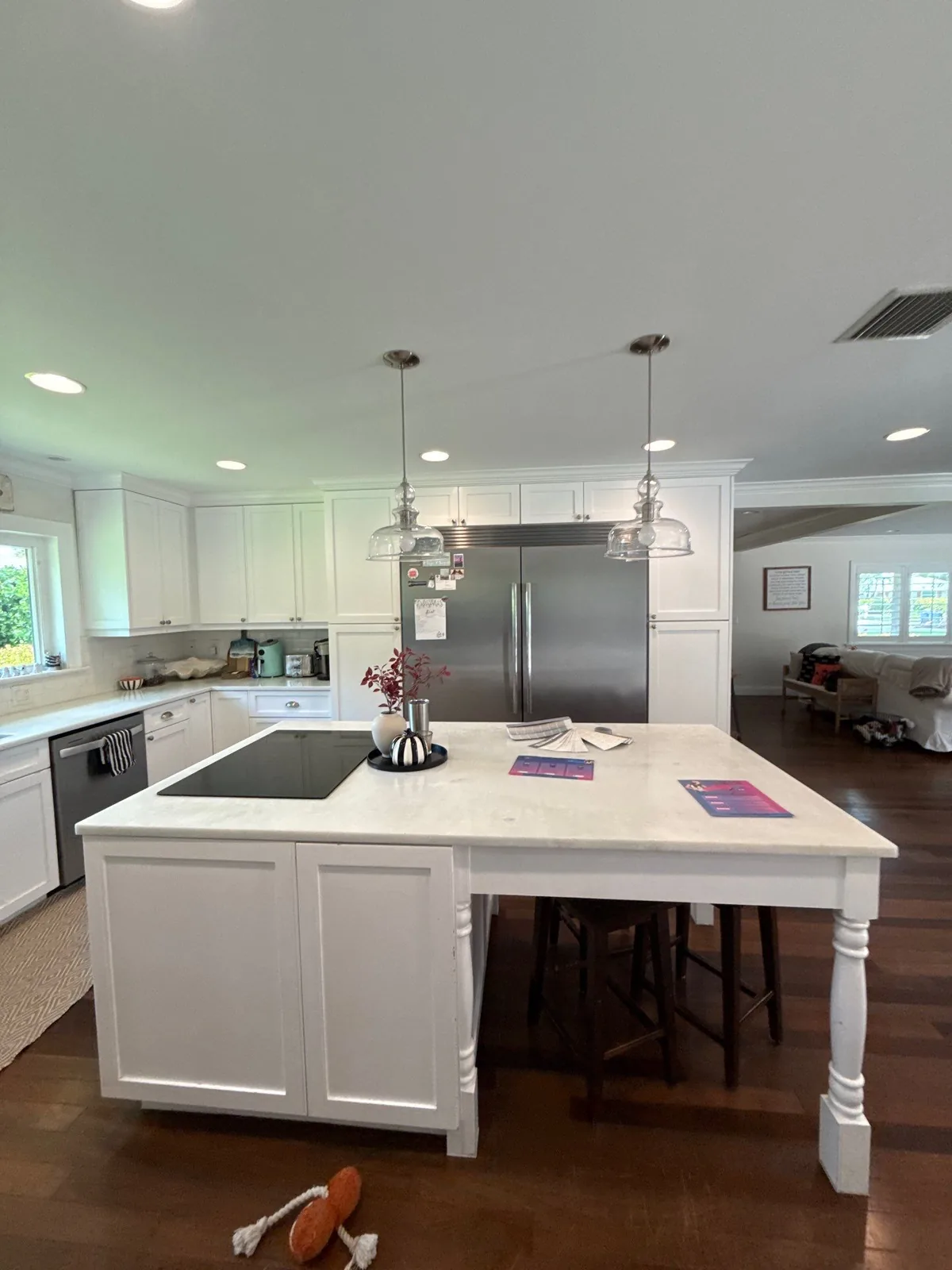 Cabinet Refinishing in North River Shores, Florida. Kitchen with white shaker cabinets, large white island with stone countertop, pendant lights and stainless refrigerator.