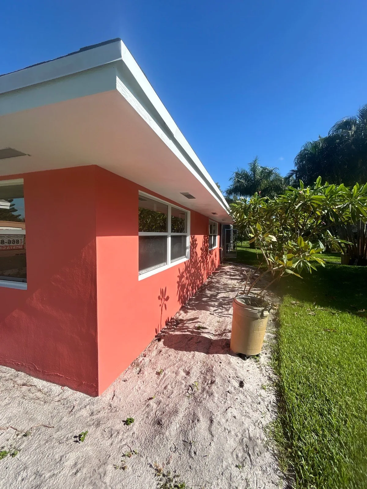 Exterior Painting in North River Shores, Florida. Single-storey home with freshly painted coral stucco walls, white fascia and white window trim under a clear blue sky.