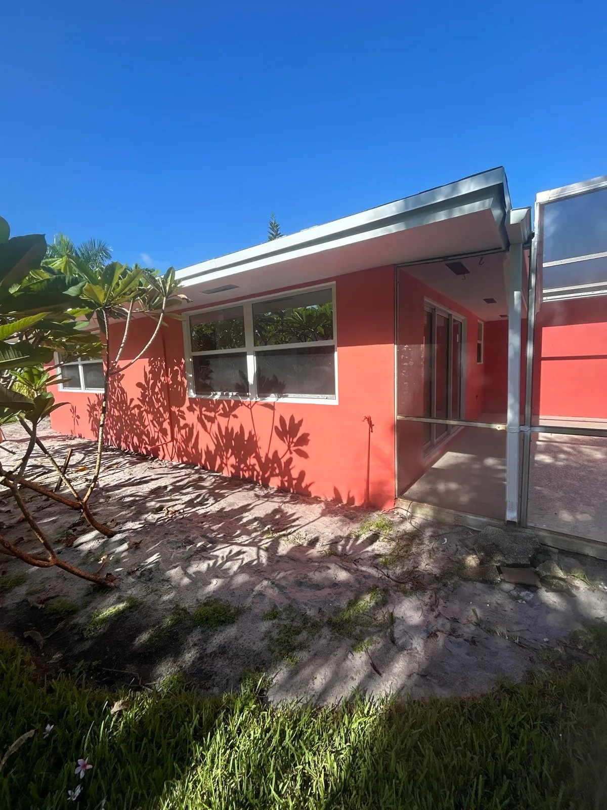Exterior Painting in North River Shores, Florida. Single-storey home with coral stucco walls and white trim, screen enclosure at right, foliage in the foreground.