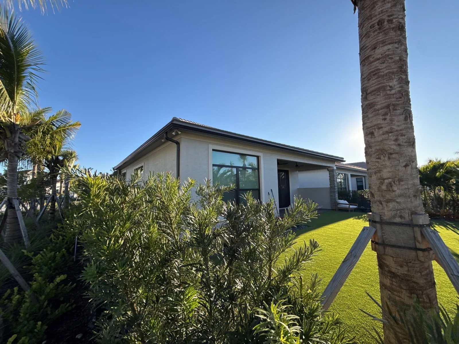 Exterior Painting in Palm Beach Gardens, Florida. Single-storey home with light stucco exterior and dark window frames, shrubs and lawn in front.
