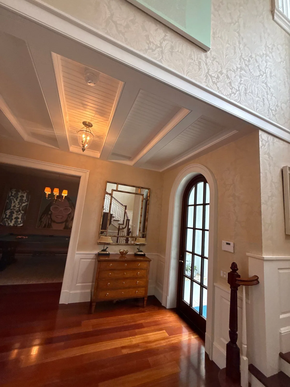 Interior Painting in Palm Beach, Florida. Entry hall with white beaded and beamed ceiling, cream textured walls, white wainscoting and an arched glazed door.