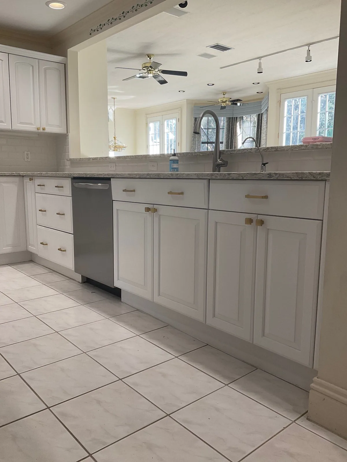 Cabinet Refinishing in Palm City, Florida. Refinished light grey kitchen base cabinets with brass pulls, stone countertop and stainless dishwasher.