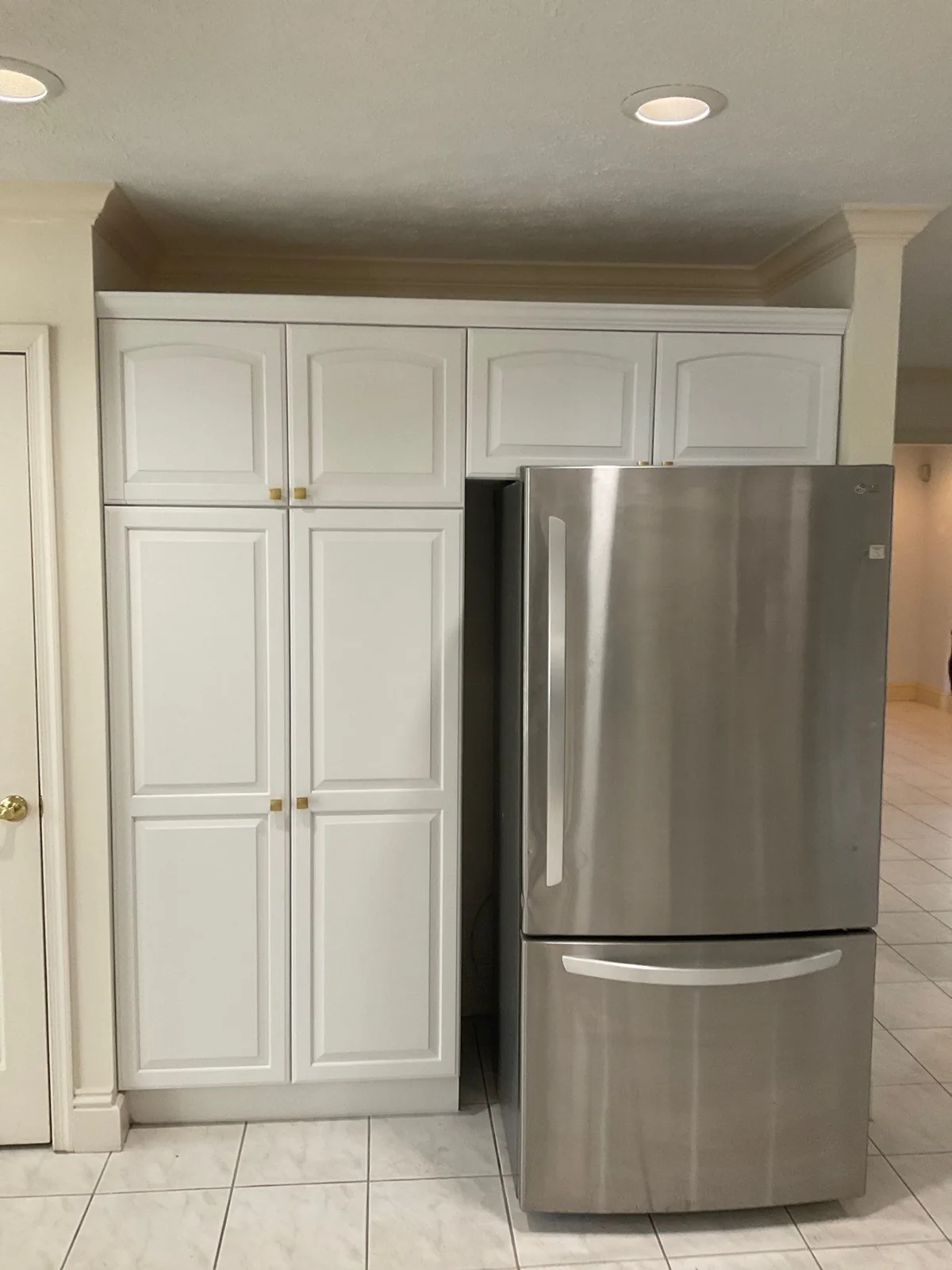 Cabinet Refinishing in Palm City, Florida. Refinished white floor-to-ceiling pantry cabinets beside a stainless steel refrigerator.