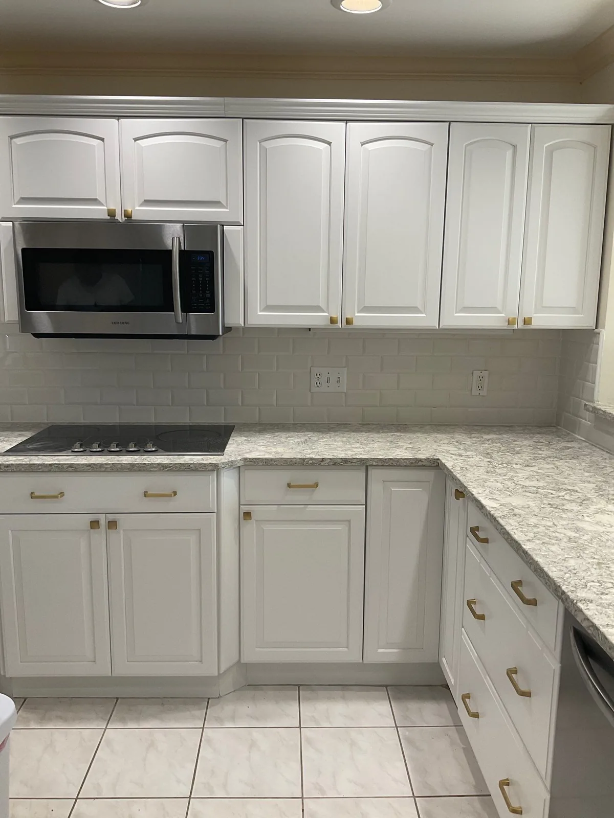 Cabinet Refinishing in Palm City, Florida. Refinished white kitchen cabinets with brass hardware, subway tile backsplash, stone countertop and stainless microwave.