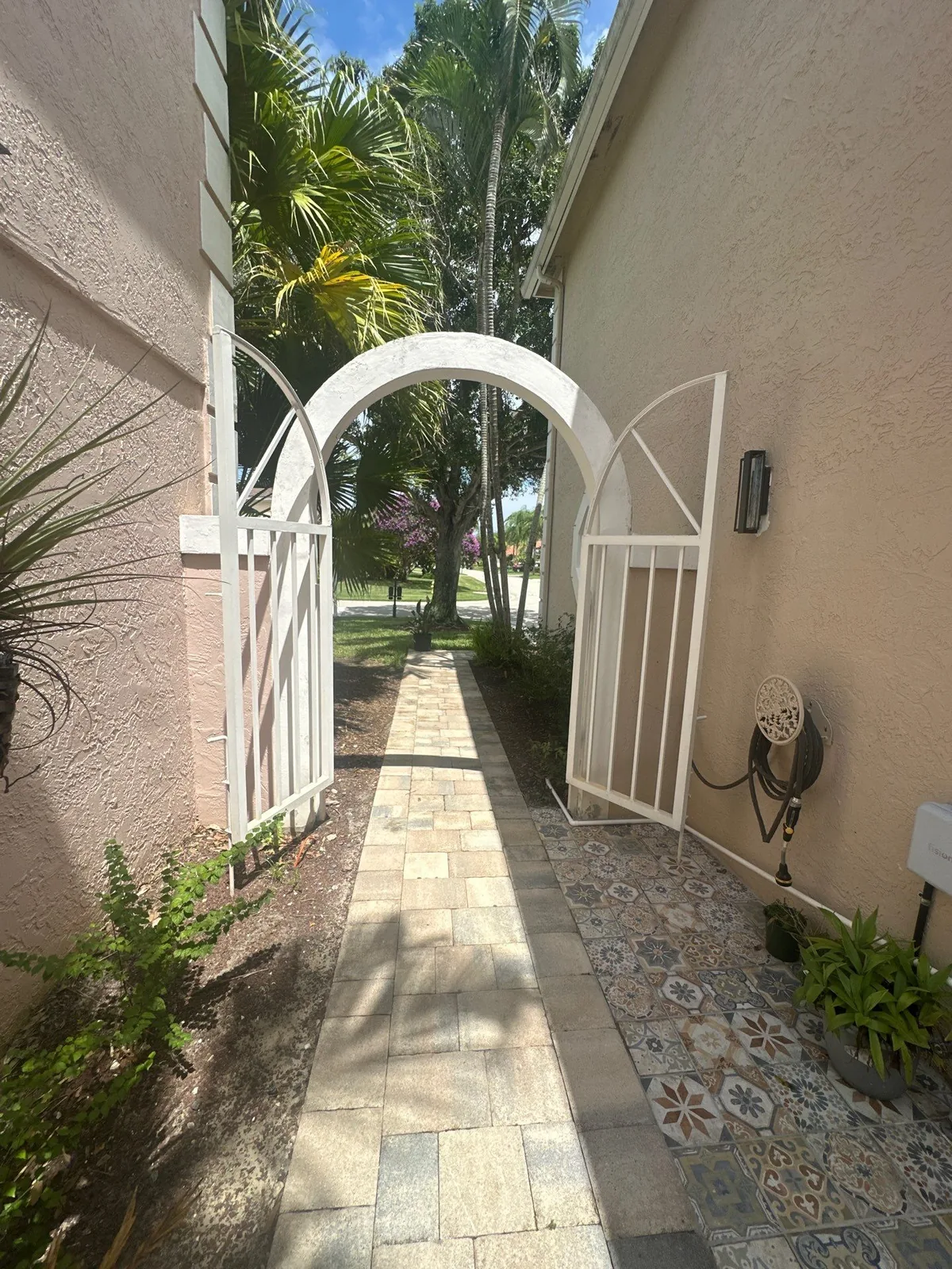 Exterior Painting in Palm City, Florida. Painted stucco side entry with a white arched garden gate and paver walkway leading to the front lawn.