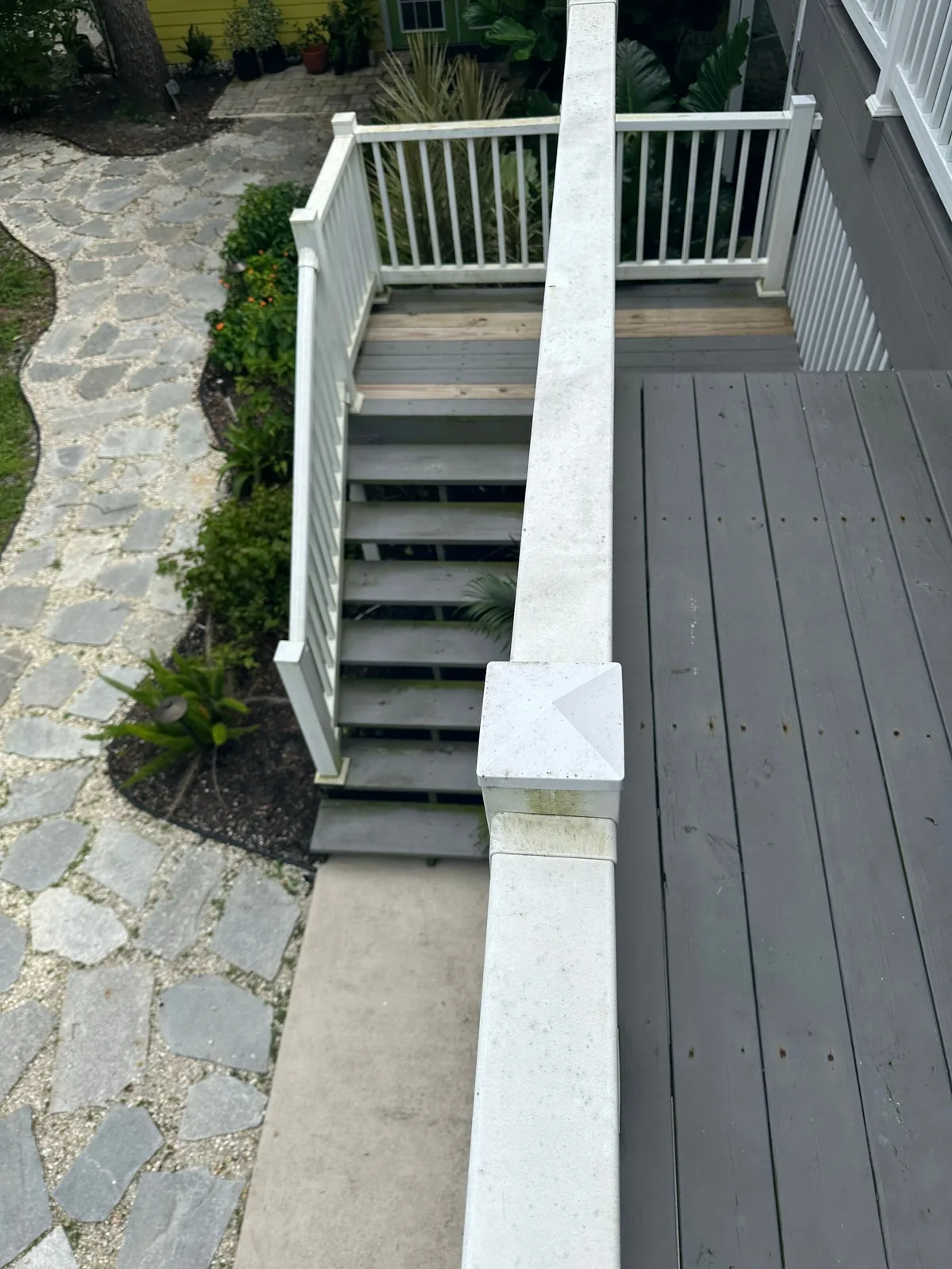 Exterior Painting in Palm City, Florida. White painted exterior staircase and railing leading to a grey painted deck, stone walkway and planting bed alongside.