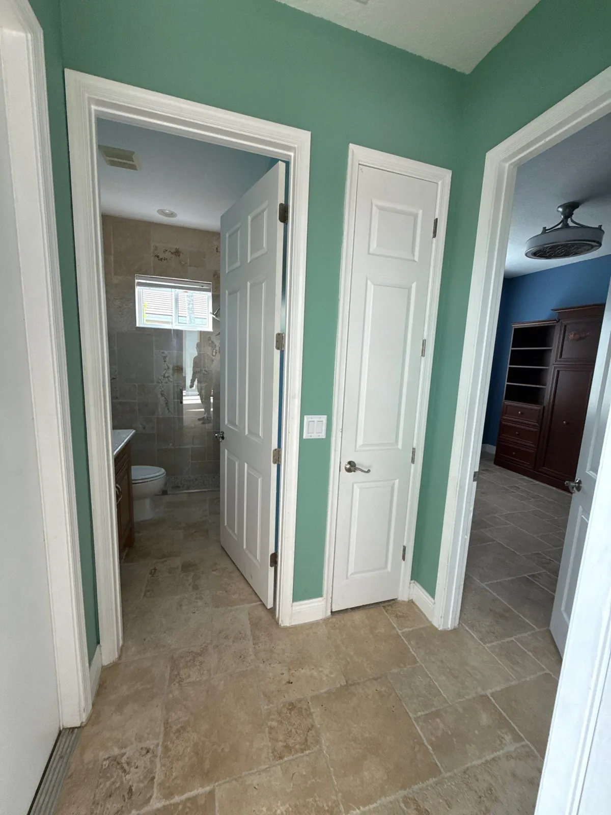 Interior Painting in Palm City, Florida. Hallway with green walls, white six-panel doors and white trim over travertine-look tile floor.