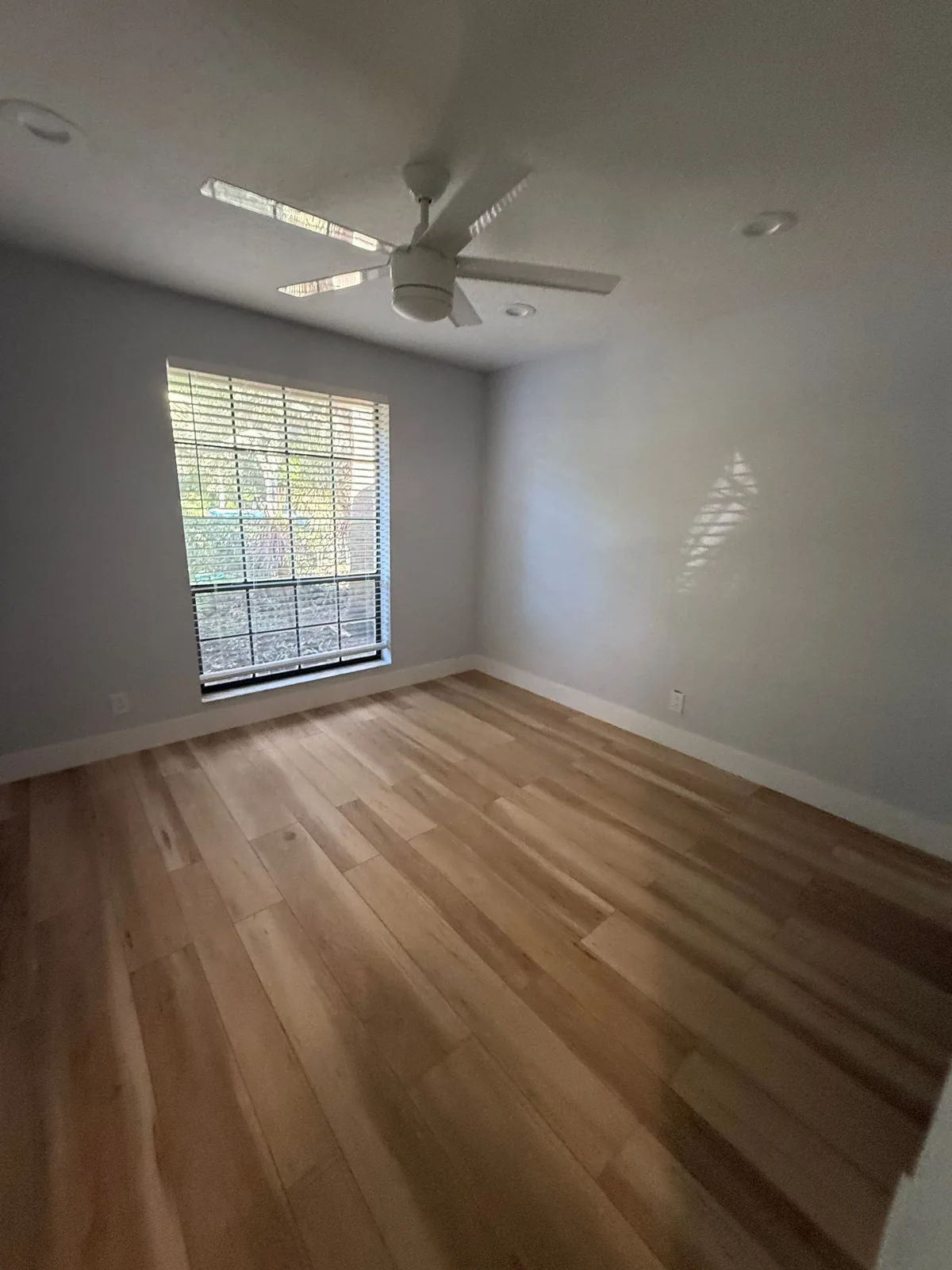 Interior Painting in Palm City, Florida. Empty bedroom with light grey walls and white ceiling, ceiling fan and single window with blinds.