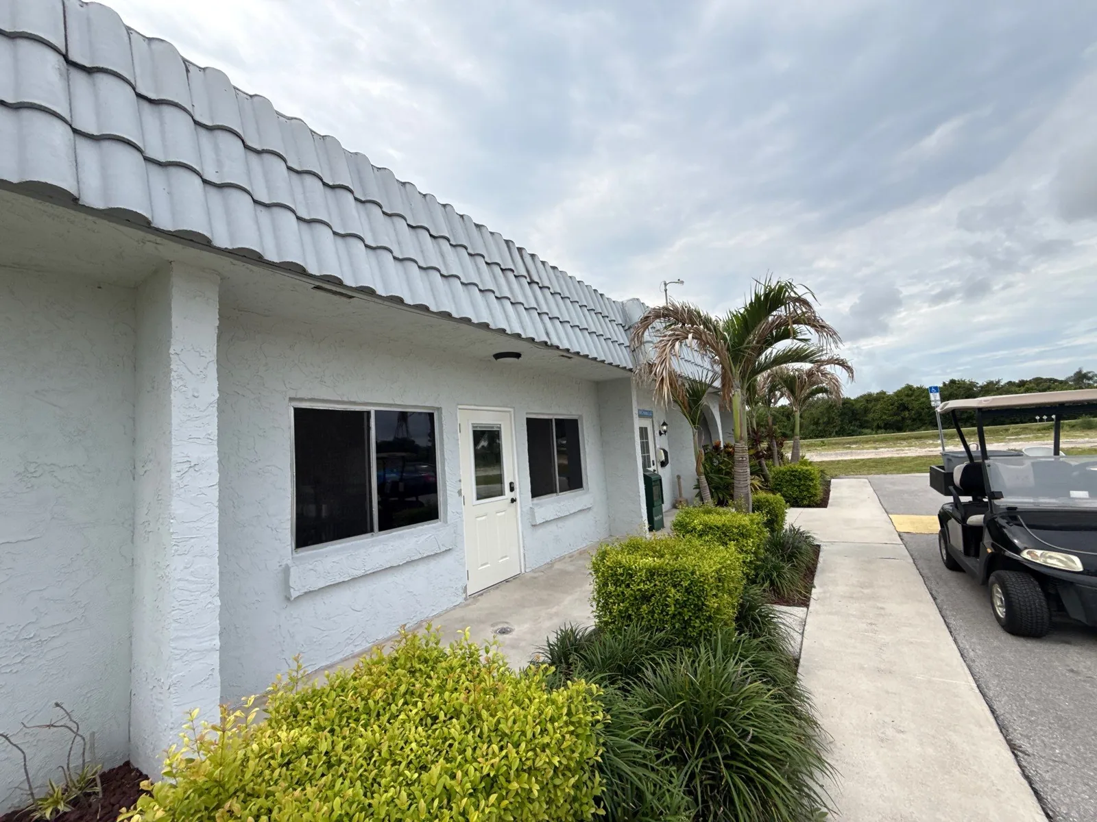Commercial Painting in Paradise Park, Florida. Single-storey commercial building with white painted stucco walls and tile roof, concrete walkway and landscaping, a golf cart parked at right.