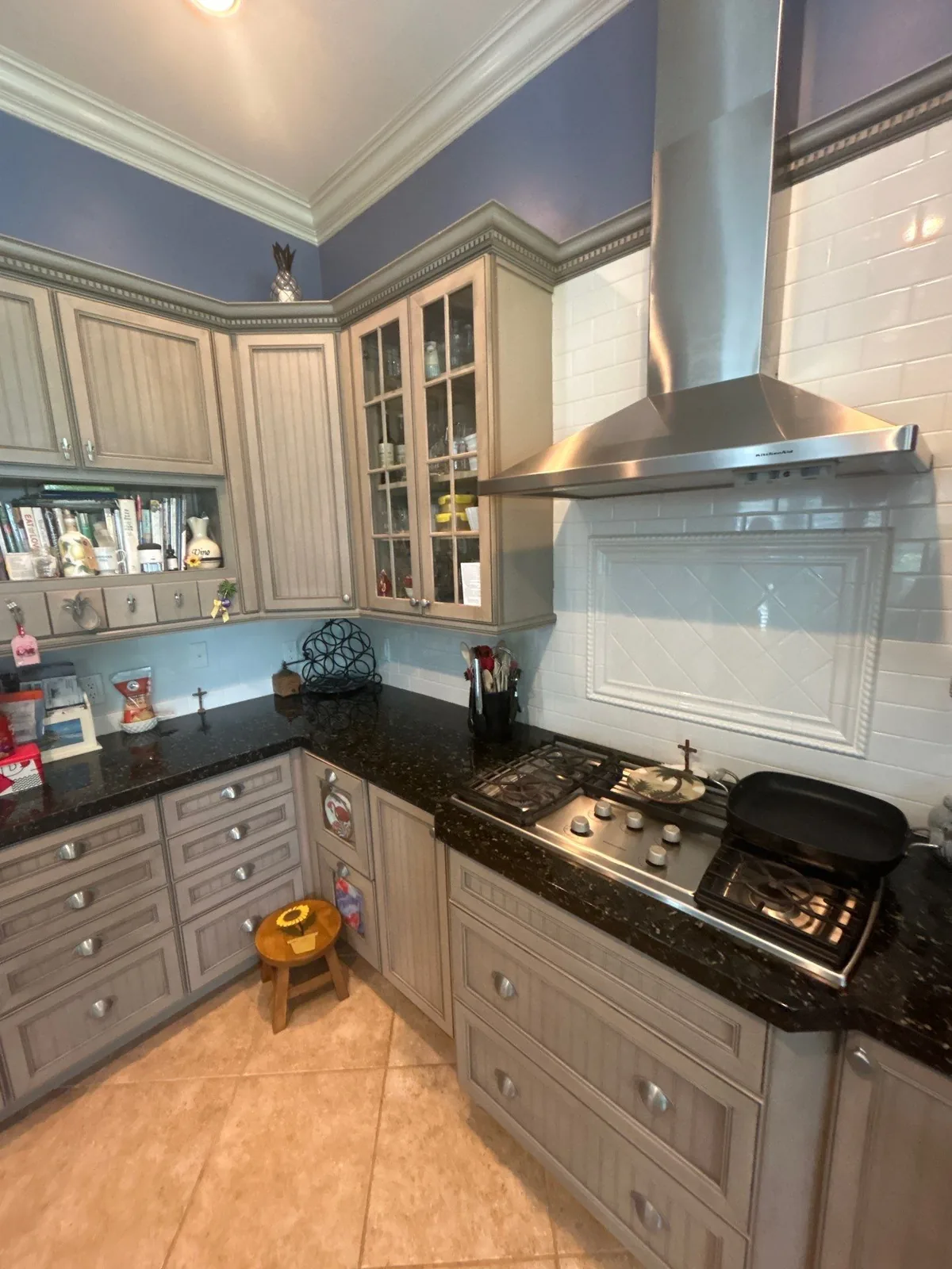 Cabinet Refinishing in Pointe West, Florida. L-shaped kitchen with taupe glazed cabinets, dark granite counters, stainless range hood and blue walls.
