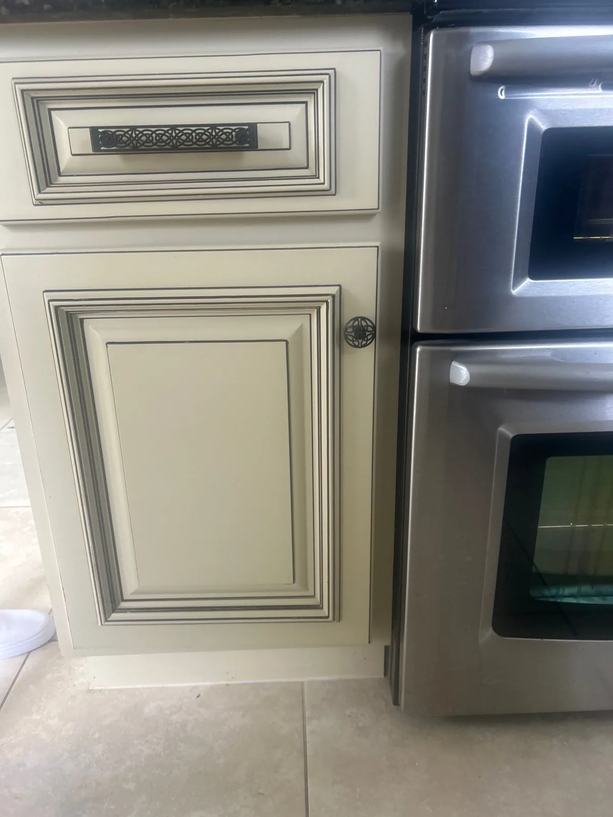 Cabinet Refinishing in Port Saint Lucie, Florida. Close-up of a refinished cream cabinet door and drawer front with dark decorative hardware, beside a stainless double wall oven.