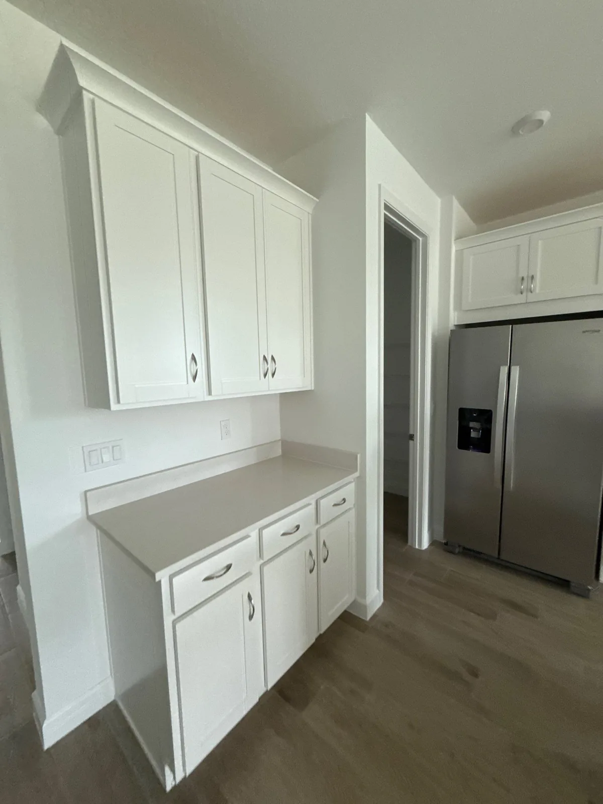 Cabinet Refinishing in Port Saint Lucie, Florida. White shaker cabinets with light countertop beside a stainless refrigerator in a kitchen with wood-look flooring.