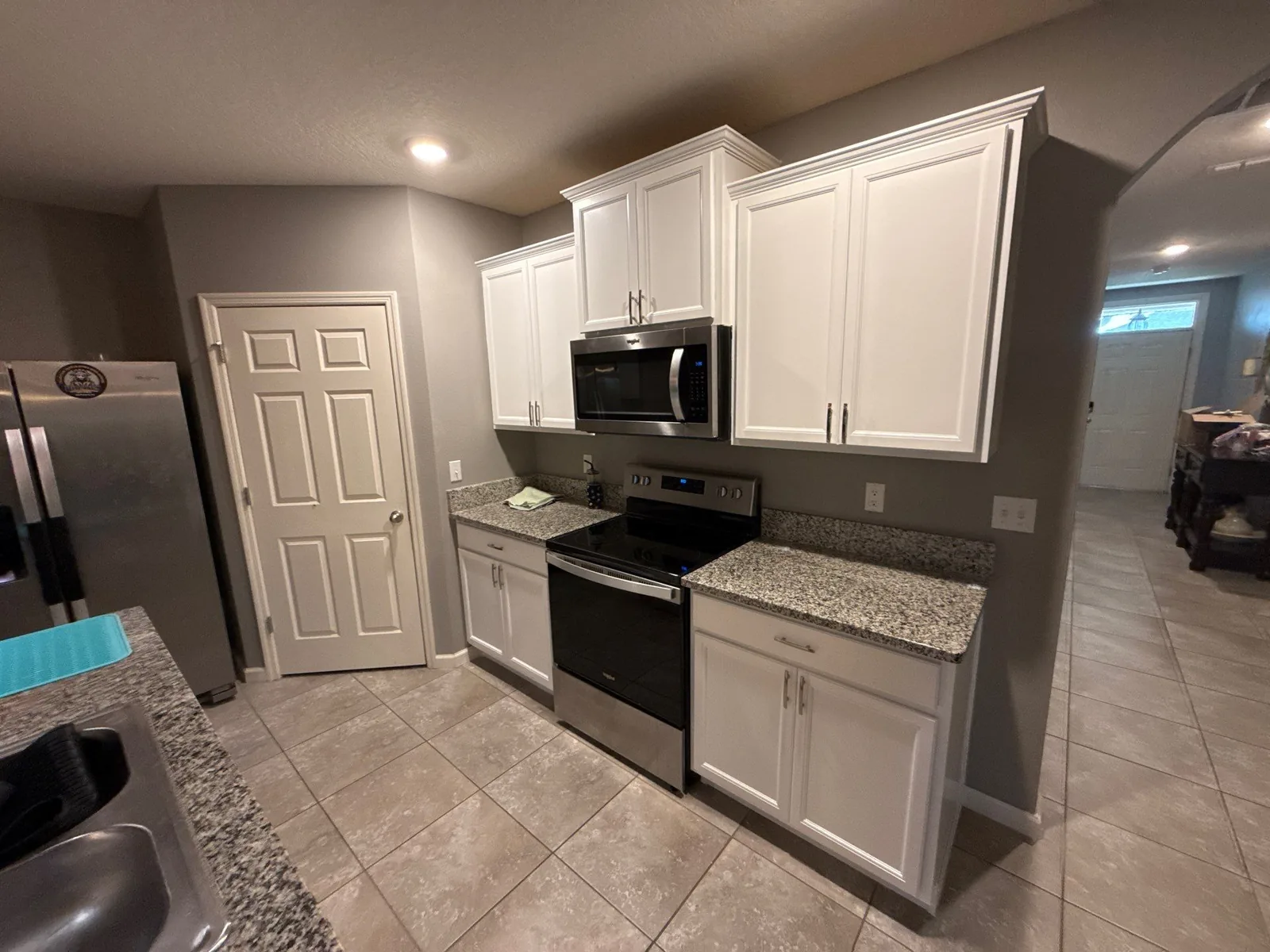 Cabinet Refinishing in Port Saint Lucie, Florida. Kitchen with white cabinets, speckled granite countertops, stainless steel range and over-range microwave, and tile flooring.