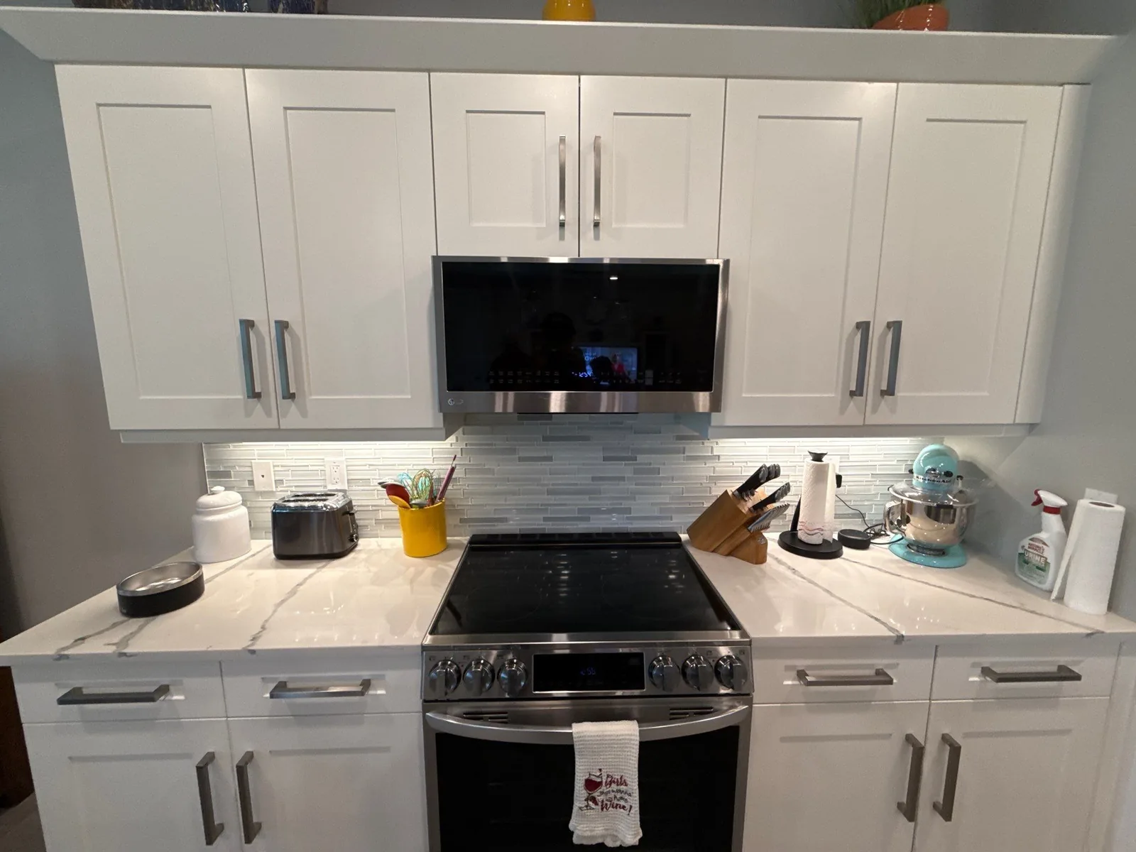 Cabinet Refinishing in Port Saint Lucie, Florida. Kitchen wall with white shaker cabinets, chrome bar pulls, tile backsplash and a stainless range and microwave.