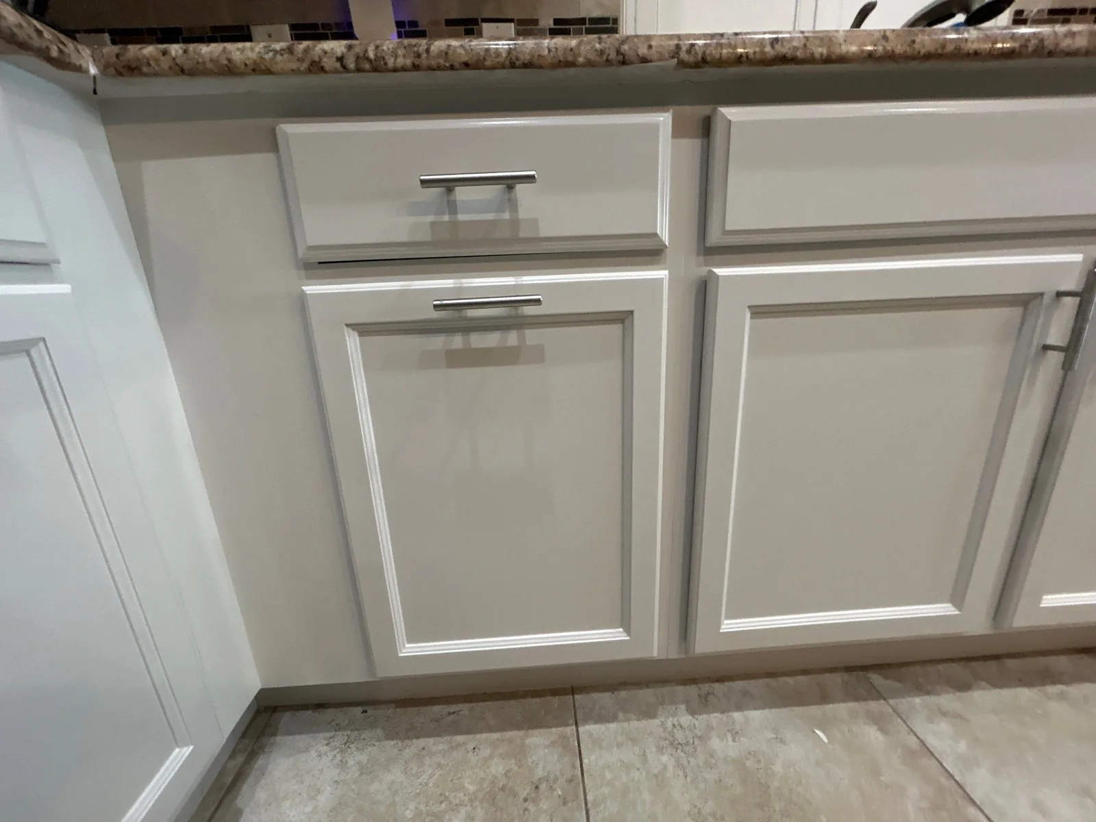 Cabinet Refinishing in Port Saint Lucie, Florida. Run of refinished light grey kitchen base cabinets and drawers with brushed metal bar pulls under a granite counter.