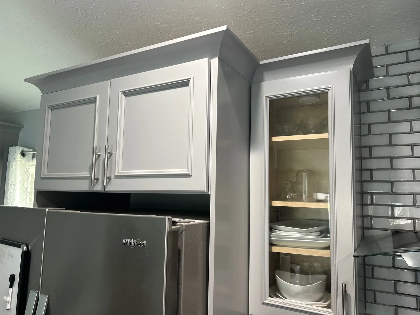 Cabinet Refinishing in Port Saint Lucie, Florida. Grey refinished upper cabinets with crown moulding and a glass-front cabinet, grey subway tile backsplash.