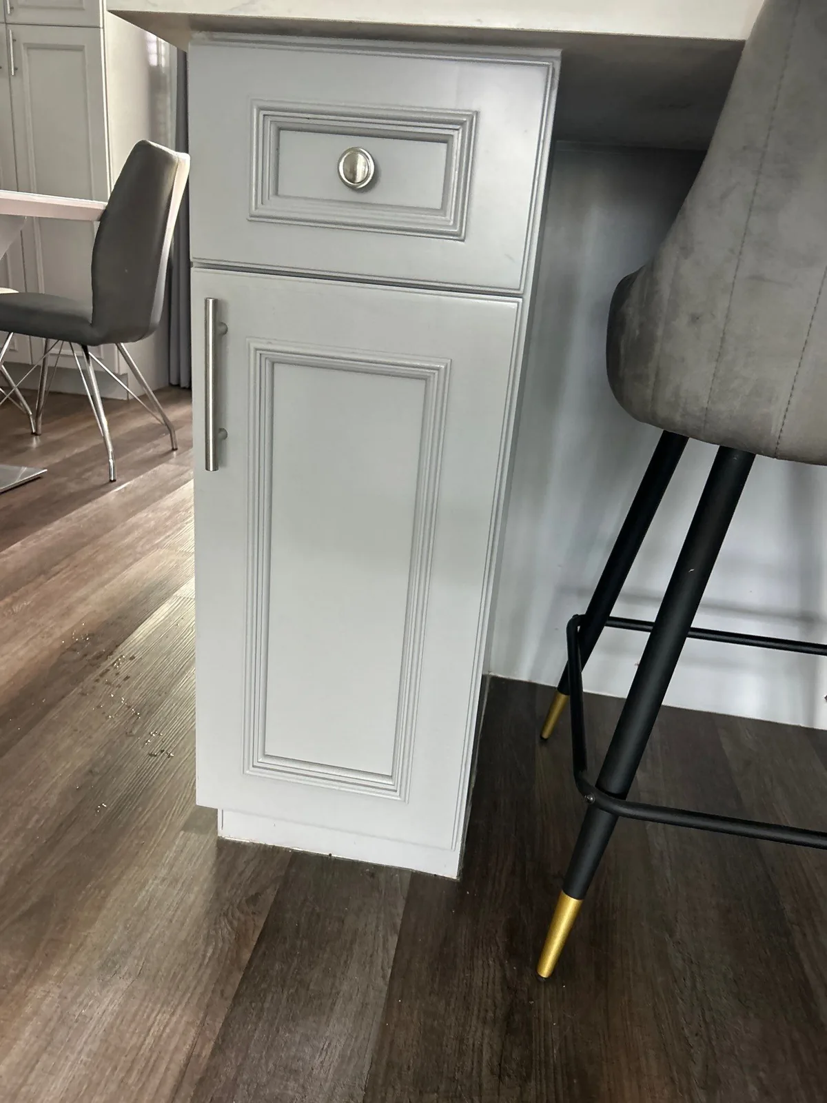 Cabinet Refinishing in Port Saint Lucie, Florida. White raised-panel base cabinet with brushed nickel pull at the end of a kitchen island, grey bar stool and wood-look flooring.