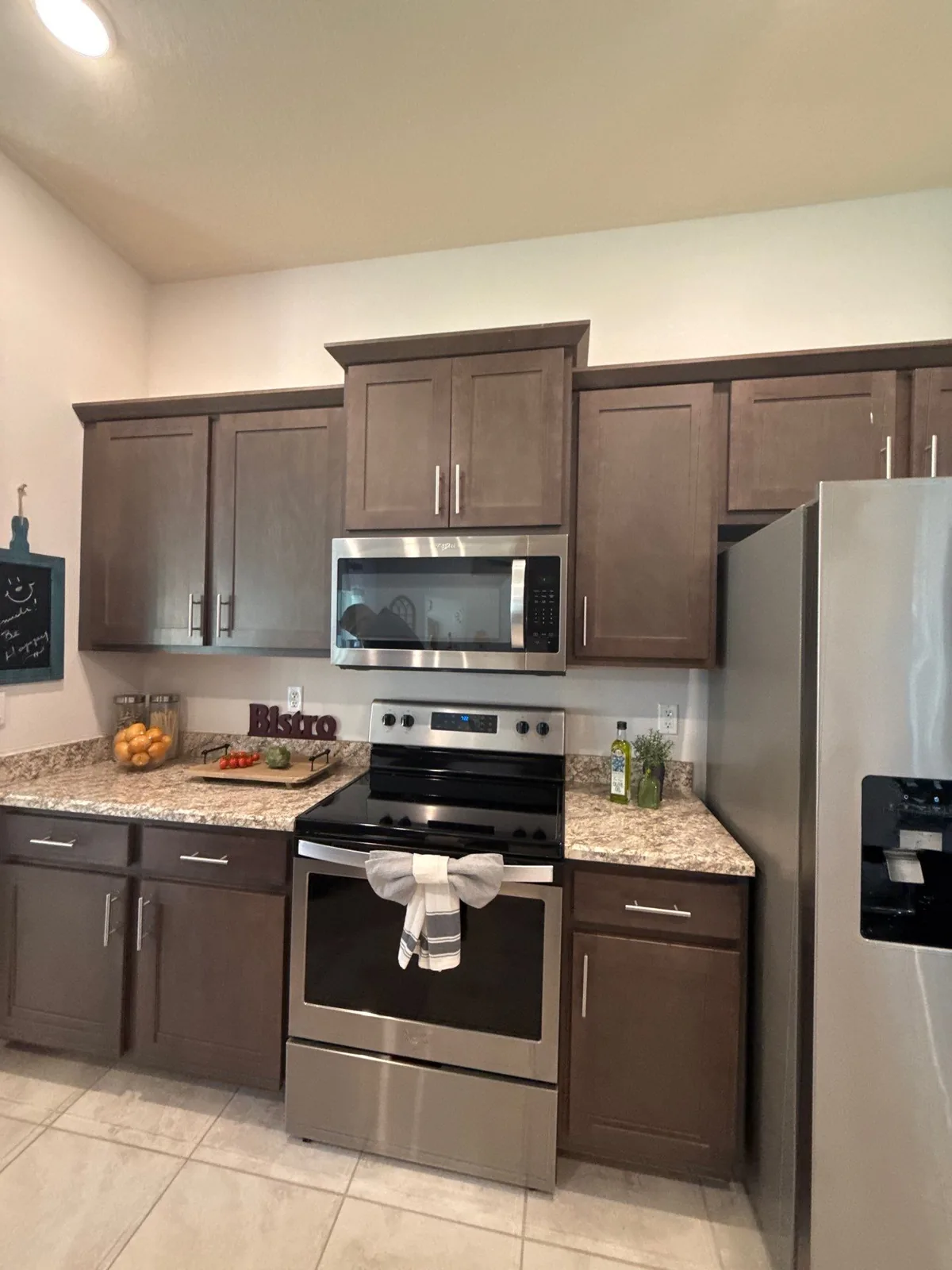 Cabinet Refinishing in Port Saint Lucie, Florida. Kitchen range wall with dark brown cabinets, granite counters, stainless range and over-range microwave.