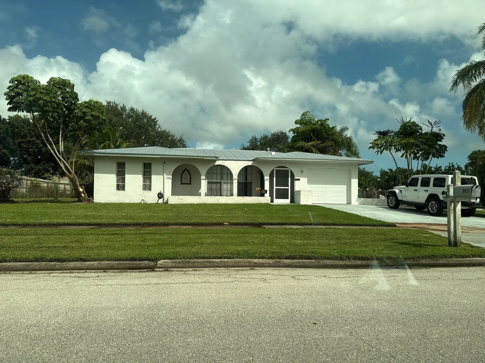 Exterior Painting in Port Saint Lucie, Florida. Single-storey house with white painted exterior, arched entry openings and attached garage, seen from the street.