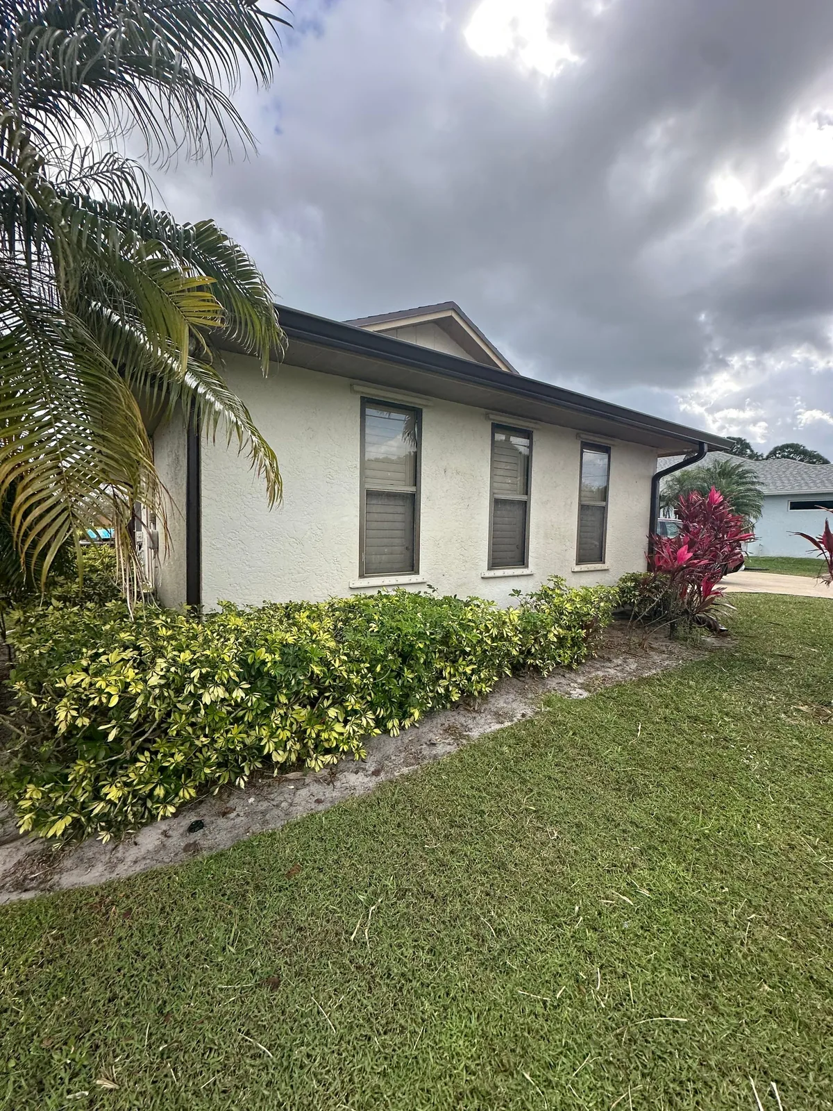 Exterior Painting in Port Saint Lucie, Florida. Side elevation of a single-storey stucco house painted cream with brown trim and fascia, hedge and lawn in front.