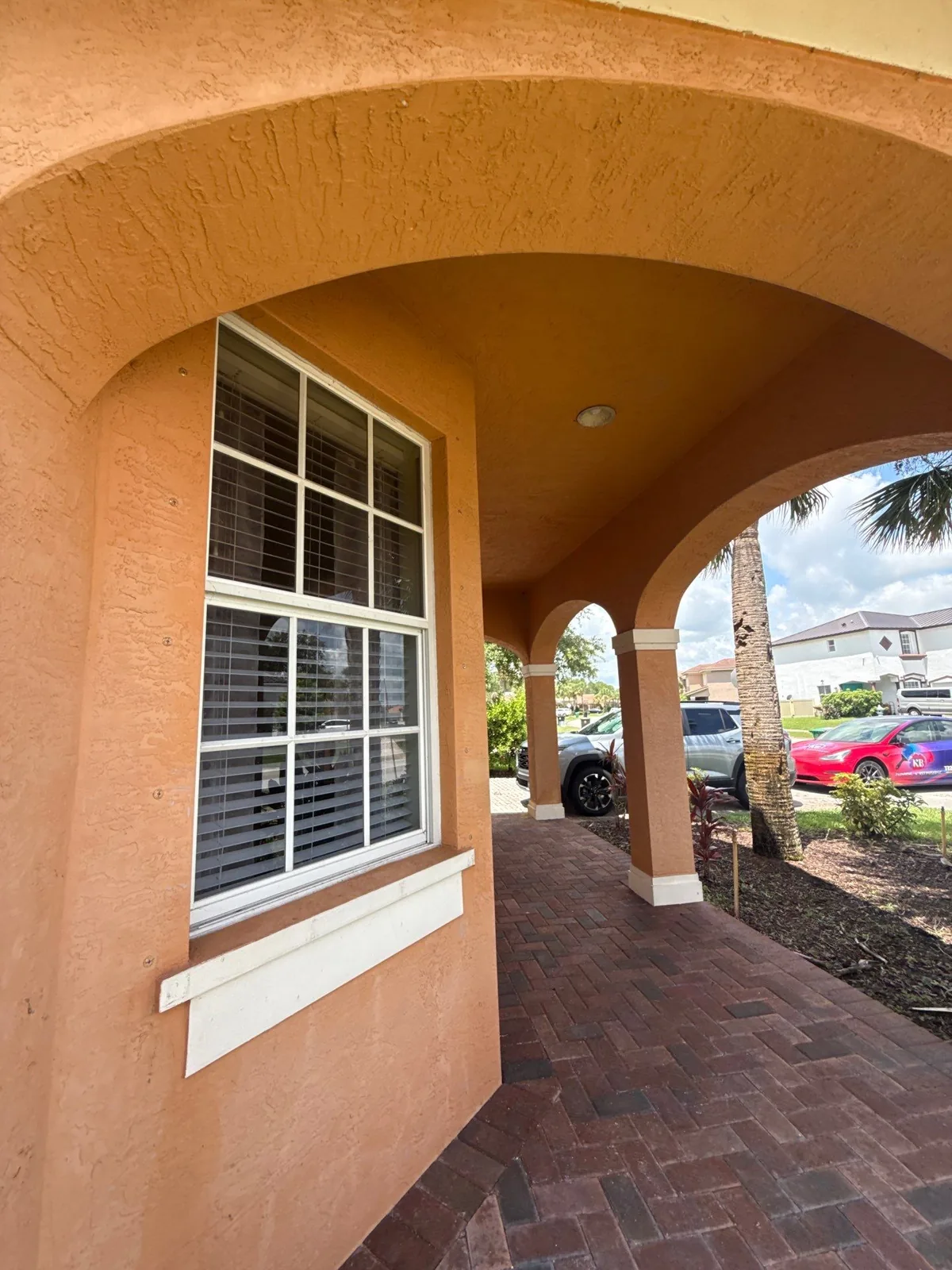 Exterior Painting in Port Saint Lucie, Florida. Arched front entry of a terracotta stucco home with white window trim and sill over a brick paver walkway.